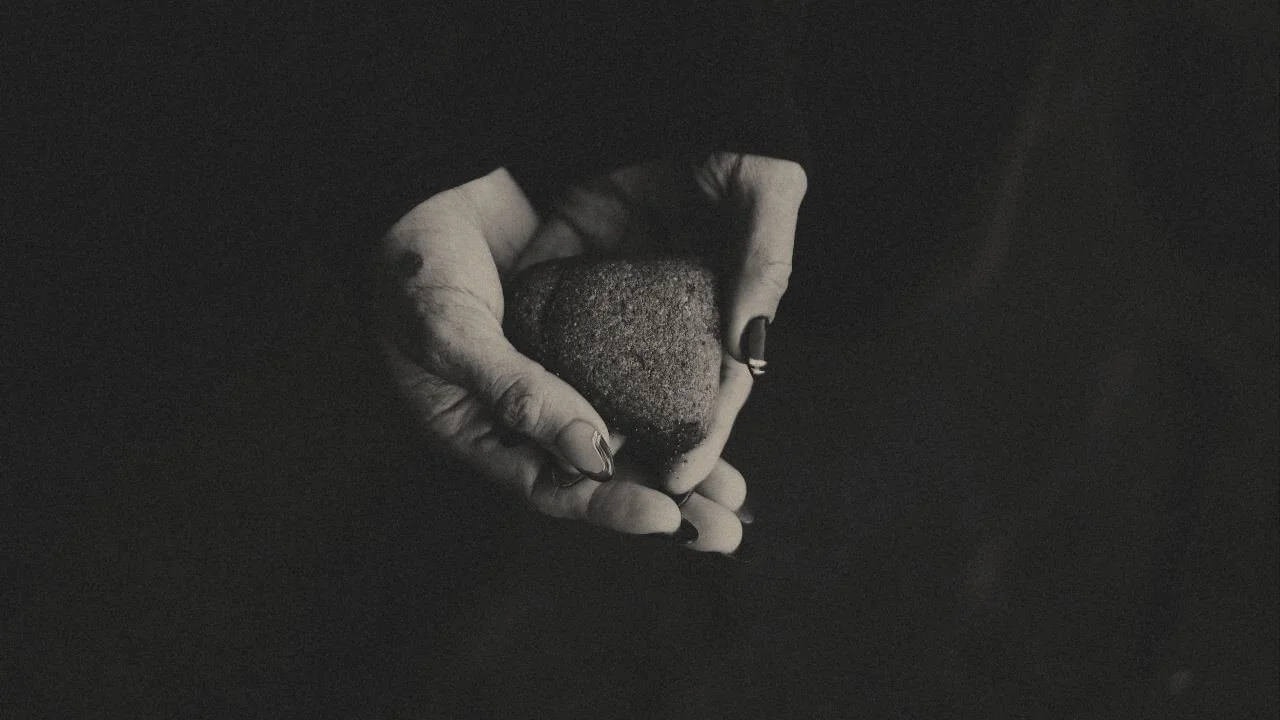 A hand gently holding a small rock against a dark background.