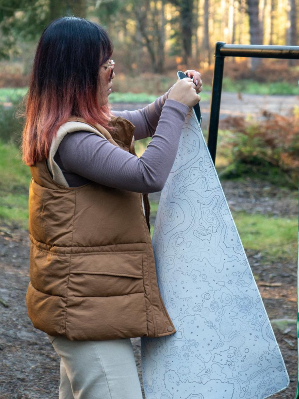 Alfina setting up our mountains by day deskpad on a stand outdoors in a forested area for our photoshoot.