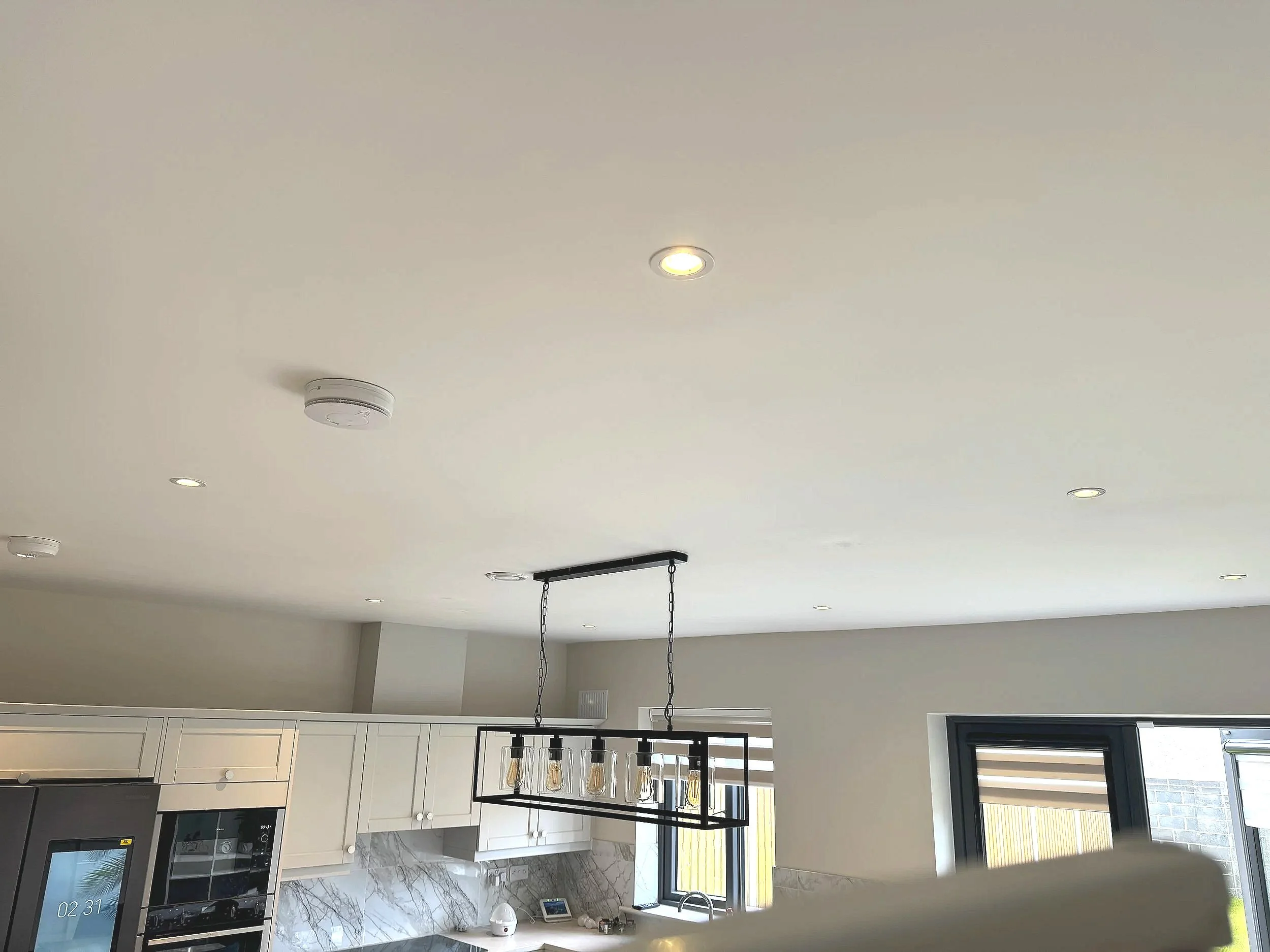 Modern kitchen with white cabinets, marble backsplash, and a rectangular black metal chandelier with five Edison-style bulbs hanging from the ceiling.