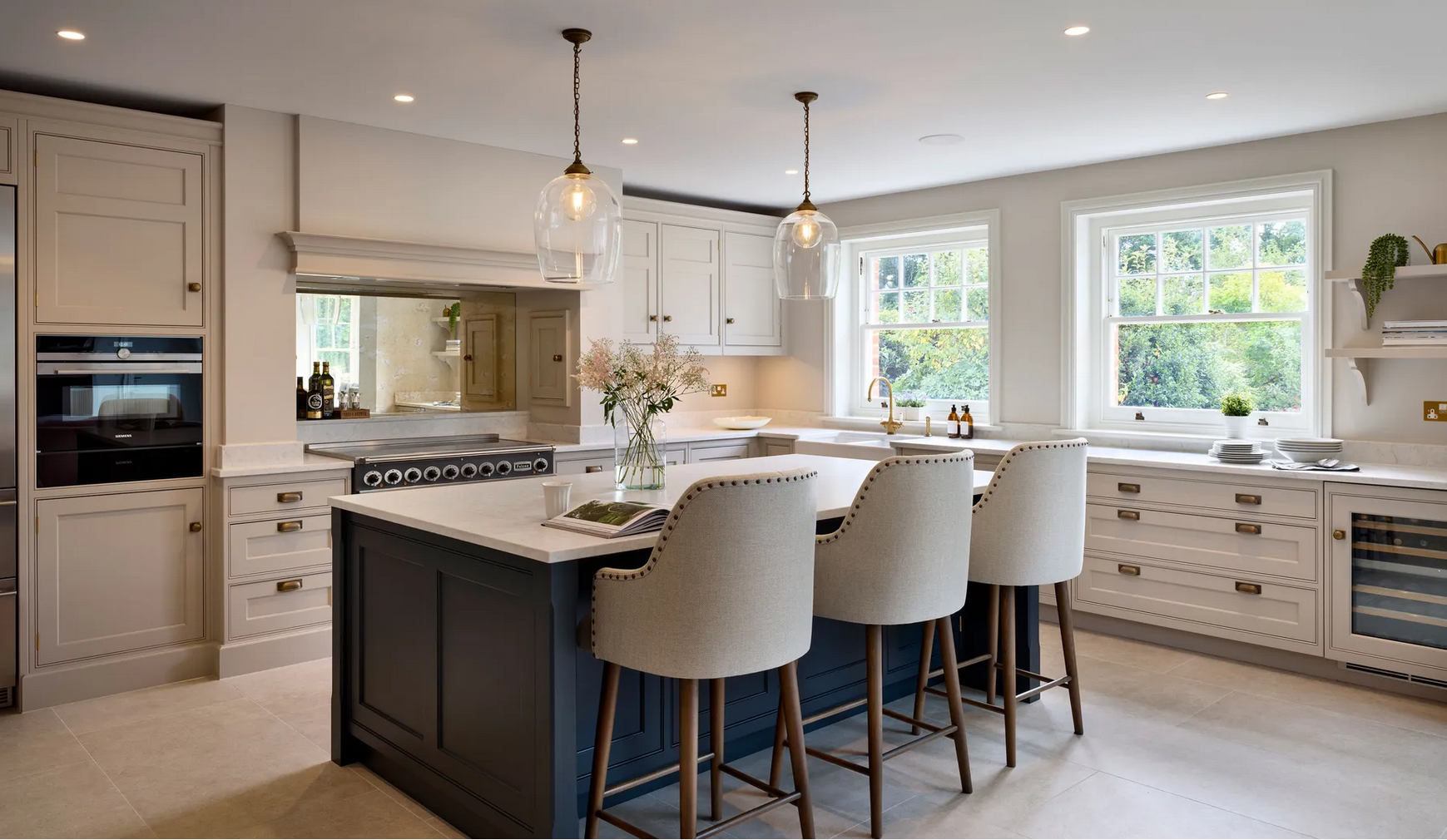 Modern kitchen with white cabinetry, large windows, a navy kitchen island with beige chairs, and pendant lights