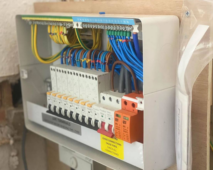 Electrical panel with colorful wiring and circuit breakers, mounted on a wall.
