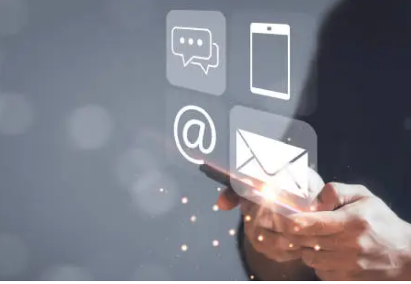 A person holding a smartphone with digital icons floating above, including a chat bubble, a smartphone, an email envelope, and an '@' symbol.