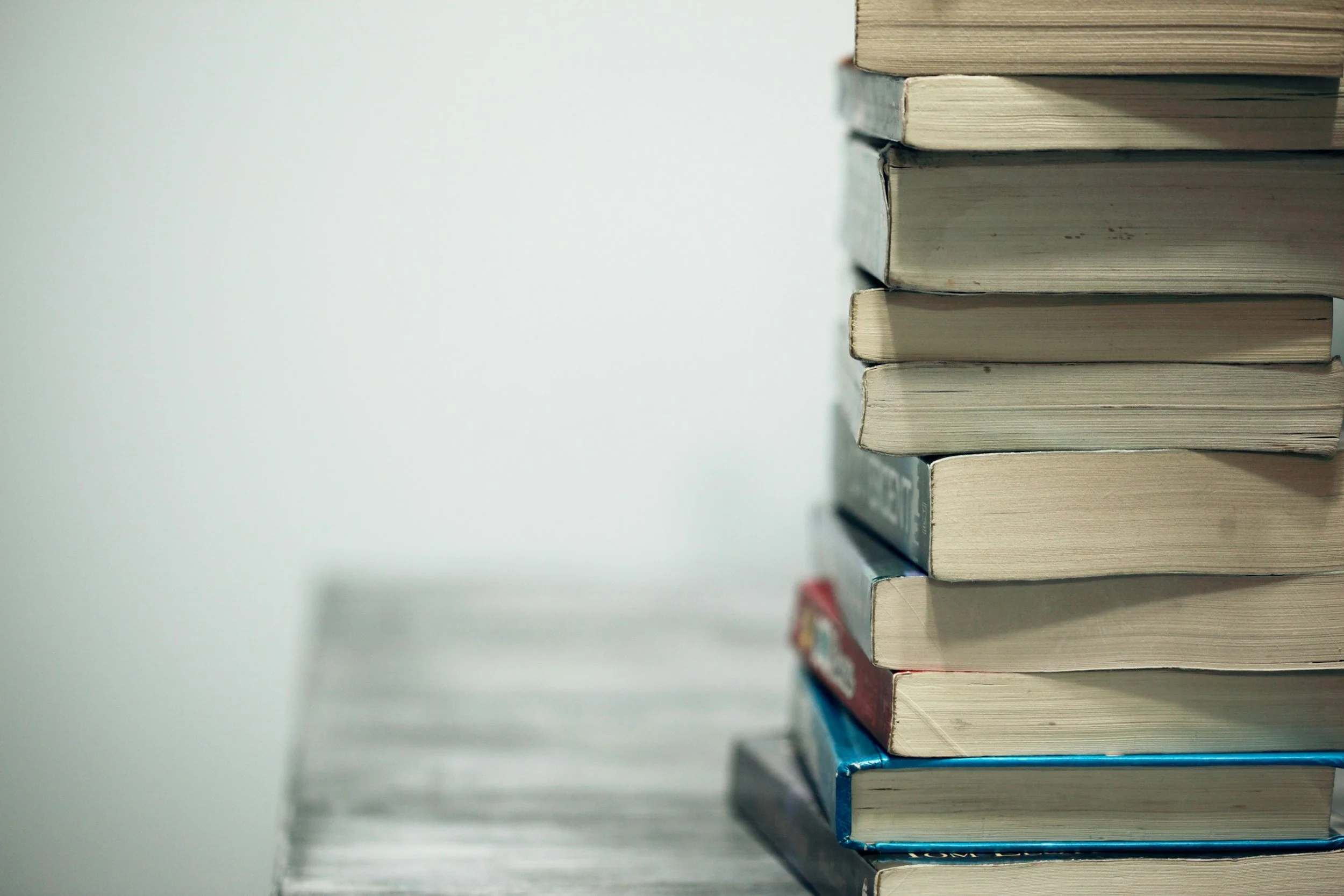 Stack of books placed vertically on a wooden surface against a plain white wall.