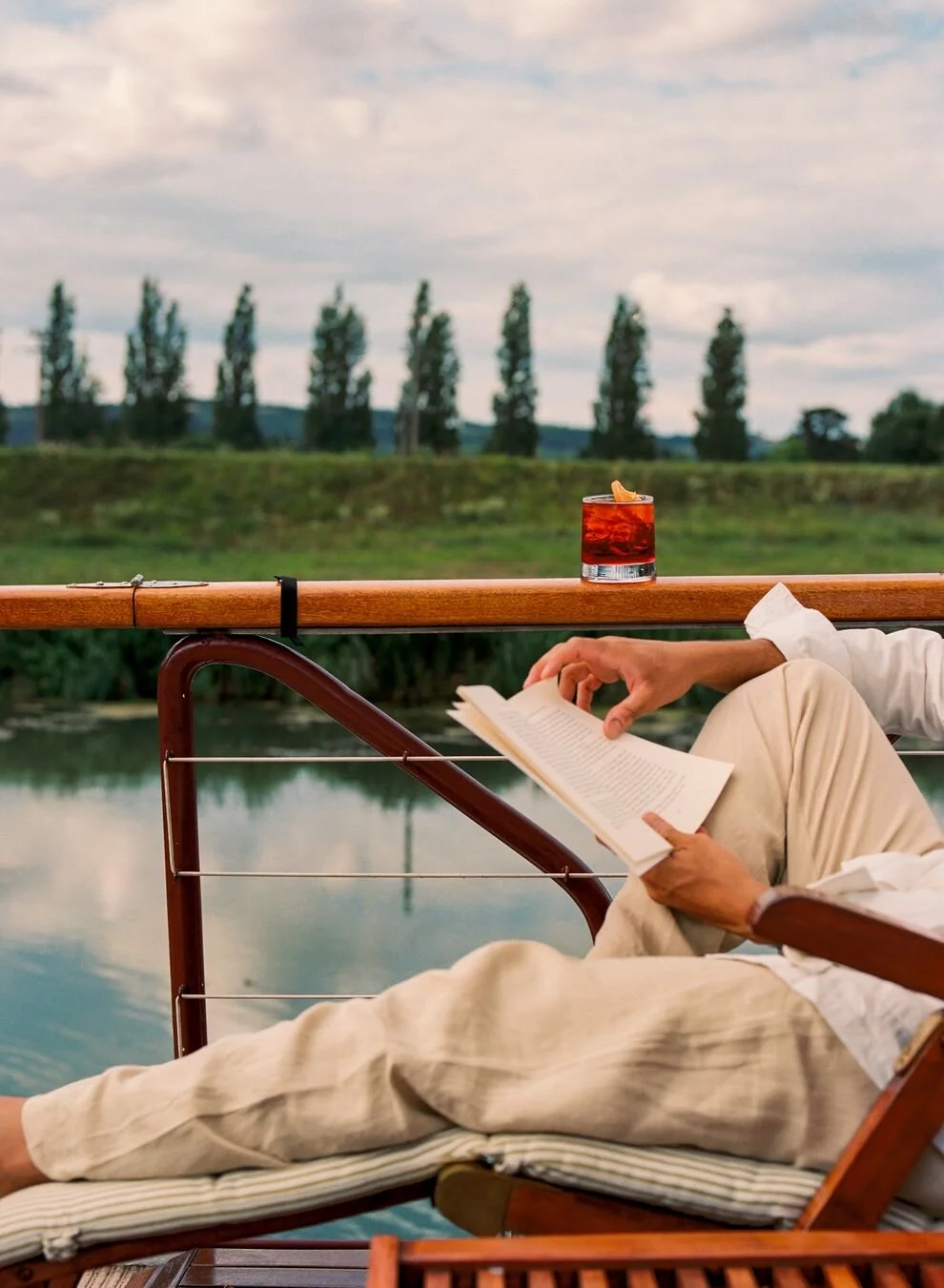A man reading a book and enjoying a negroni drink overlooking a canal