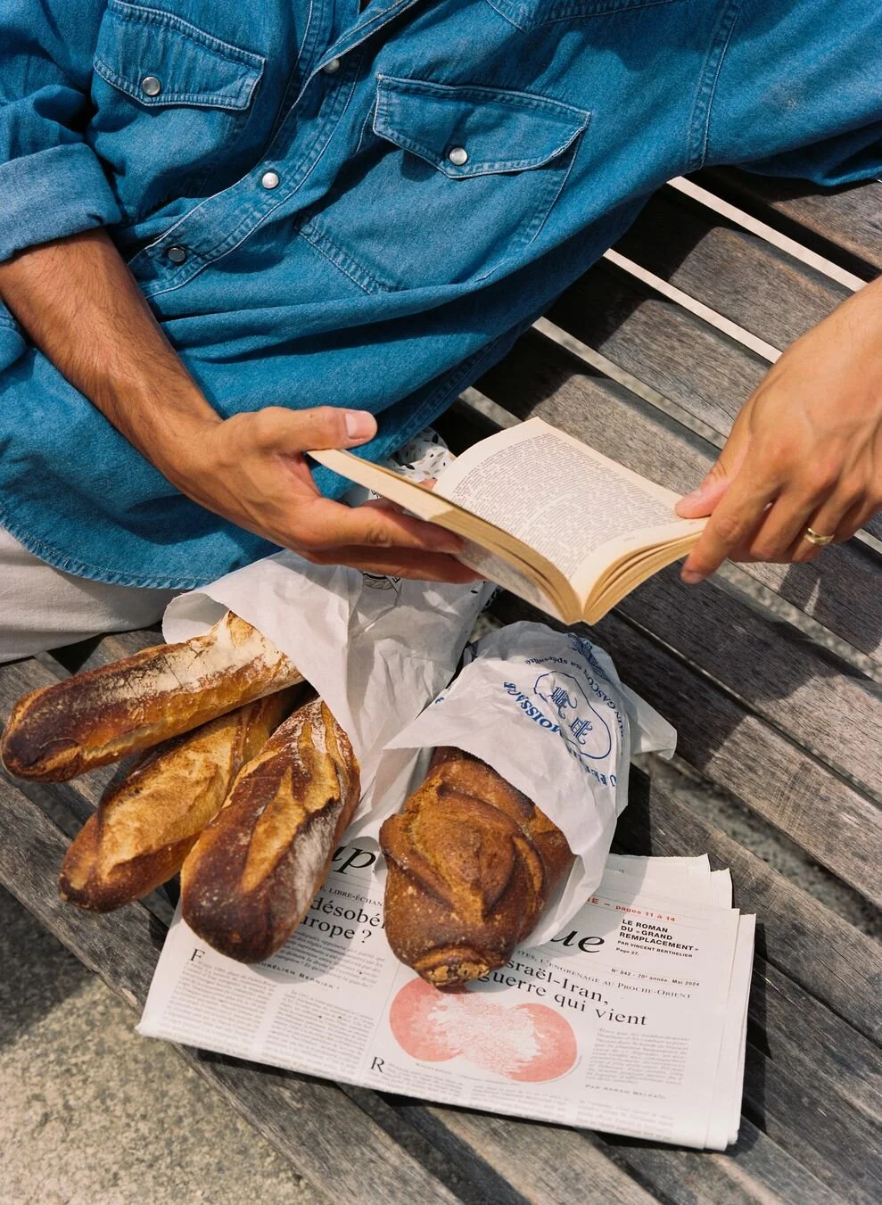 a man reading a book whilst sitting with four French baguettes