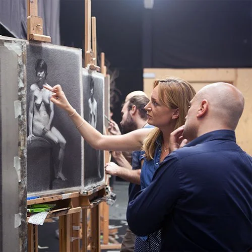 Group of people observing and working on charcoal drawings of nude models on canvas at an art studio.