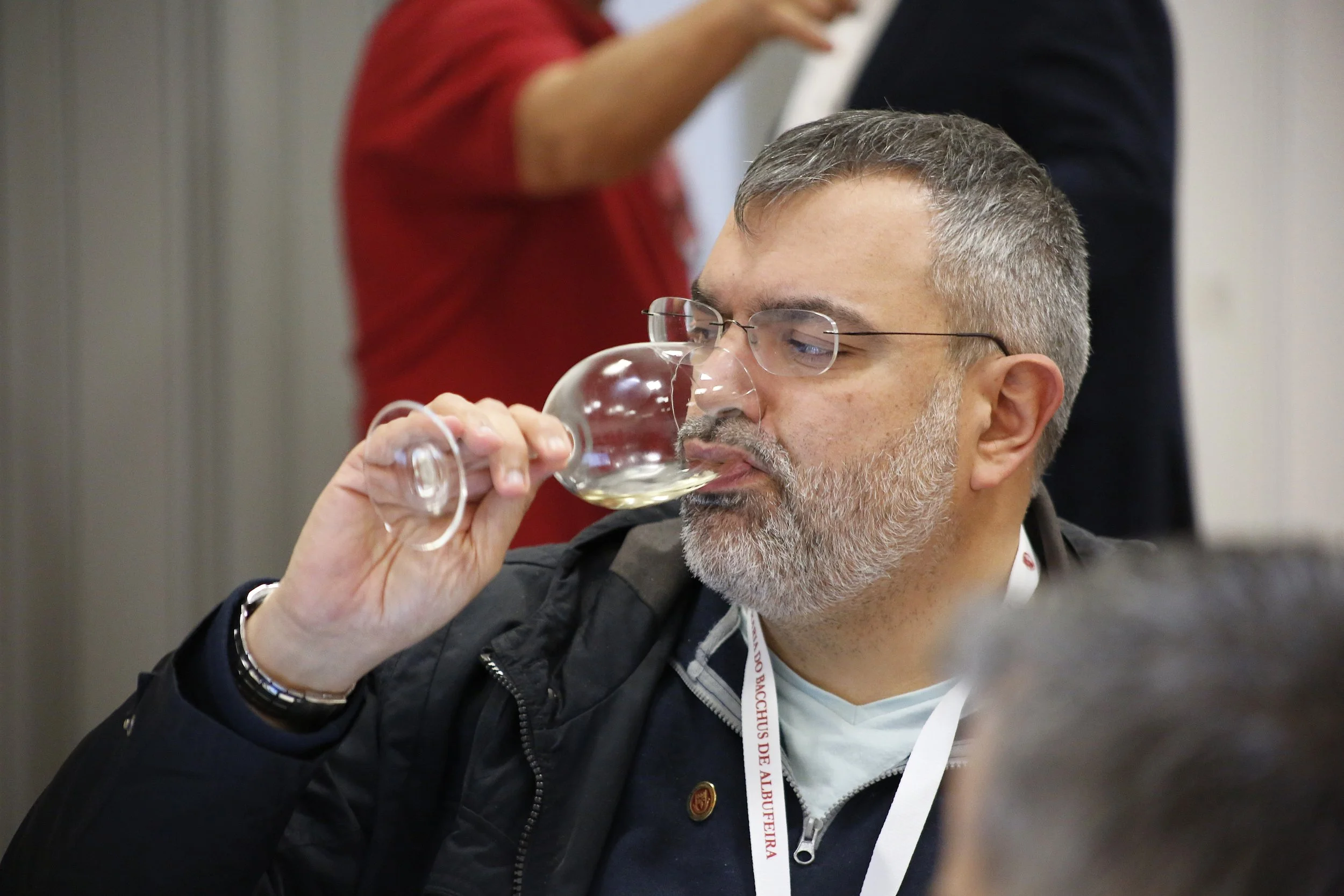 Homem com barba grisalha e óculos bebendo vinho de uma taça