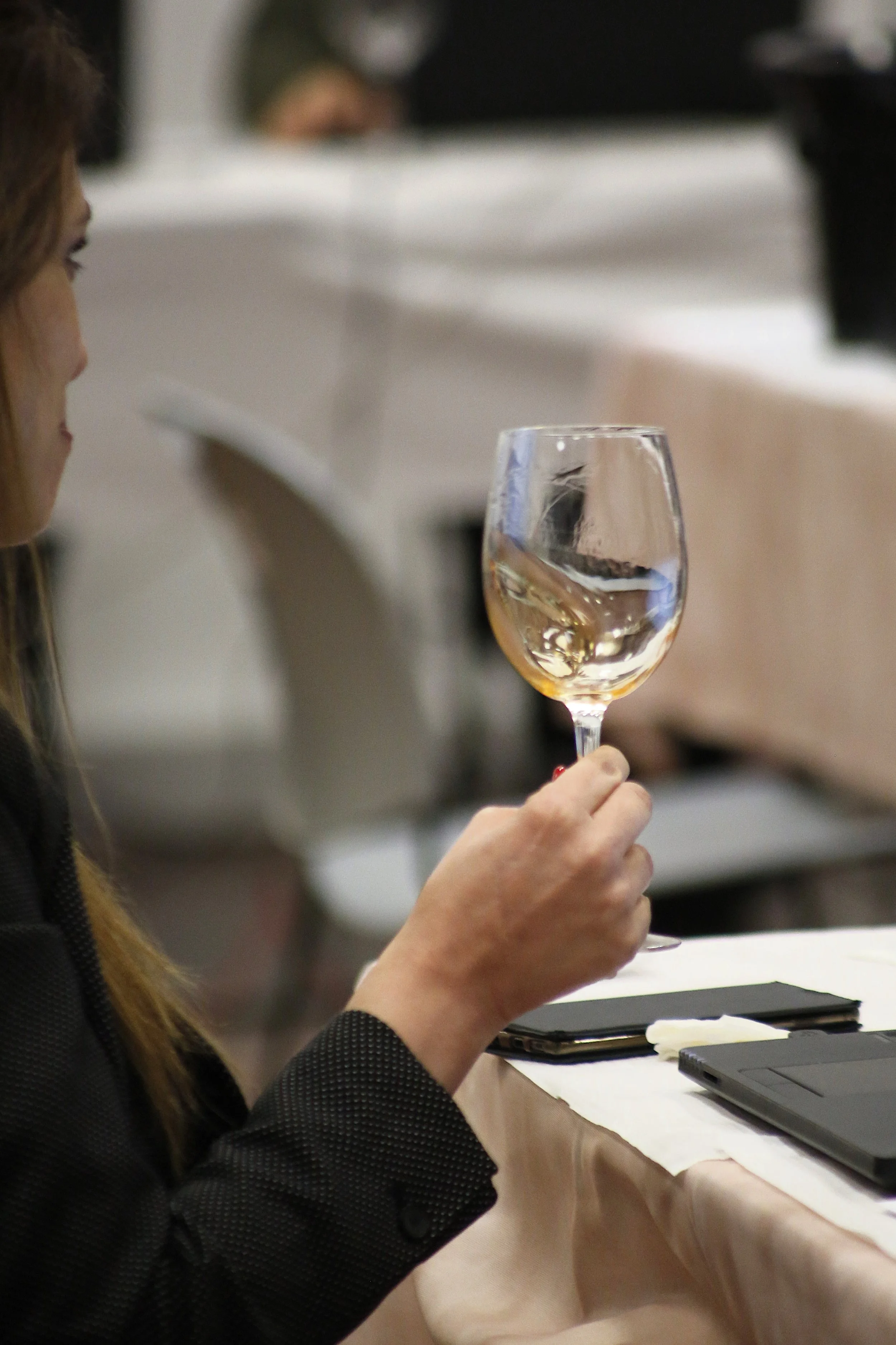 Pessoa segurando um copo de vinho branco em um ambiente interno, possivelmente em um evento ou reunião.