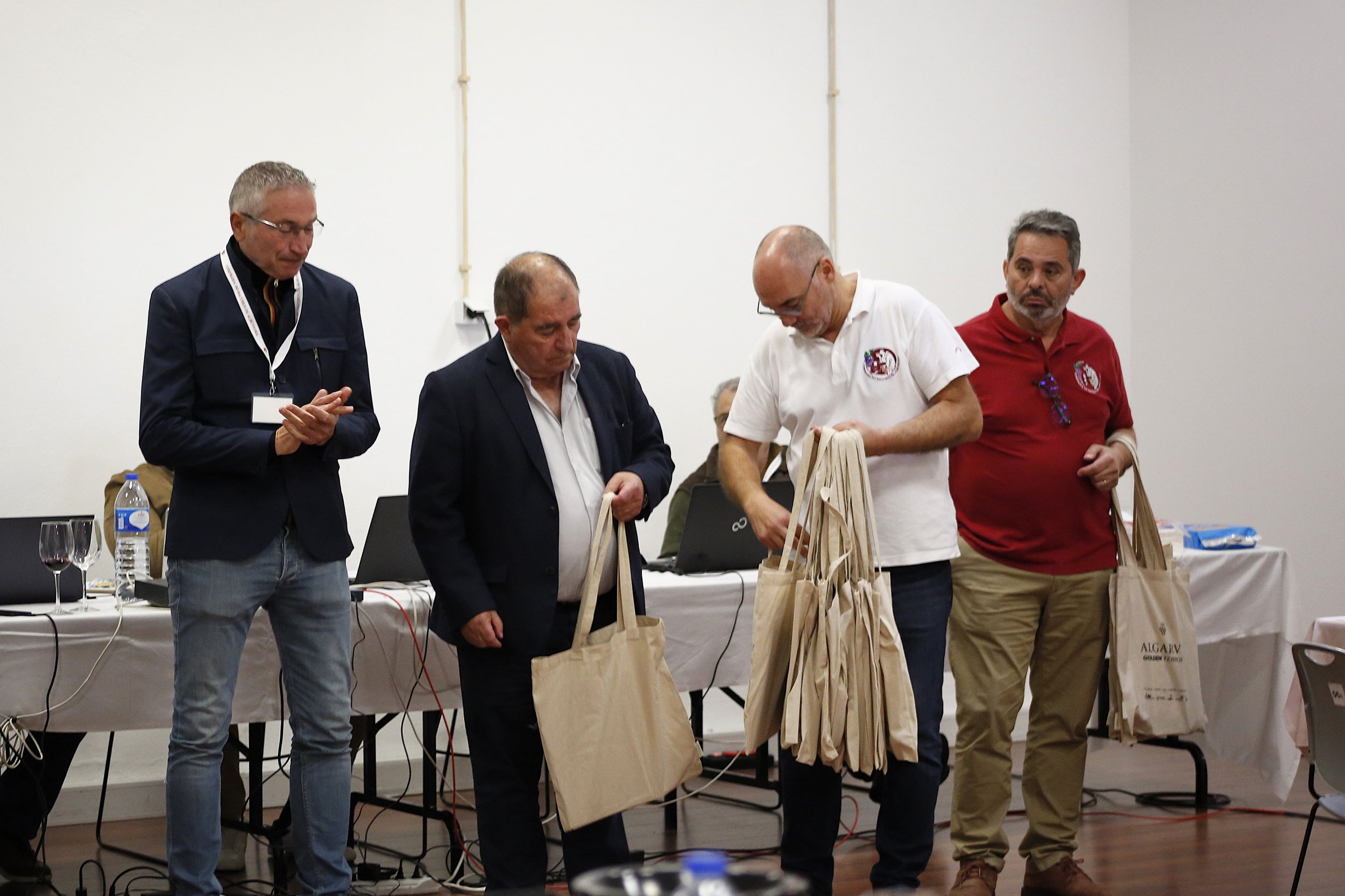 Quatro homens em uma sala, segurando sacolas de papel de tela, em uma reunião ou evento.