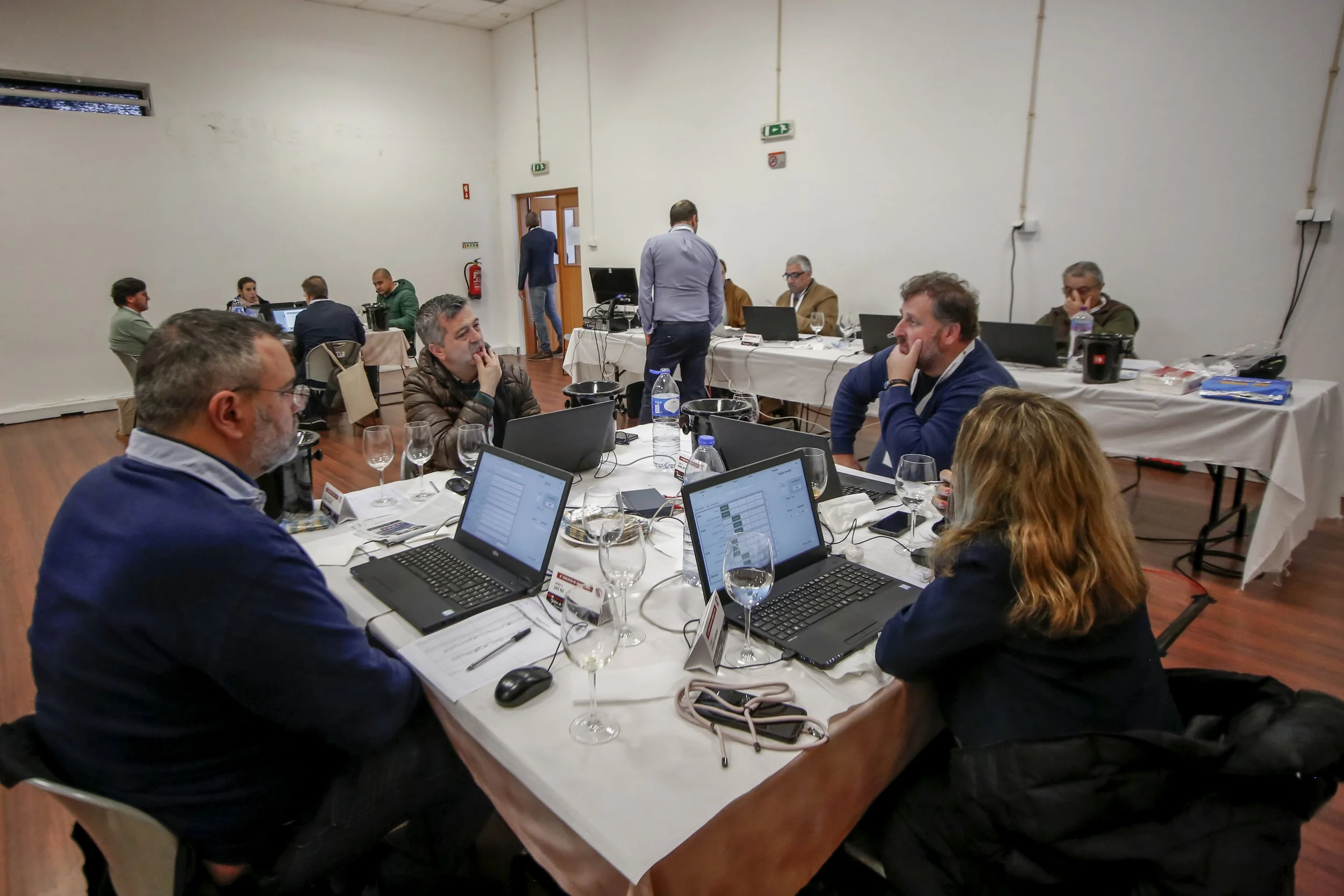 Reunião de pessoas em sala com computadores e garrafas de água em uma mesa, discutindo e interagindo.