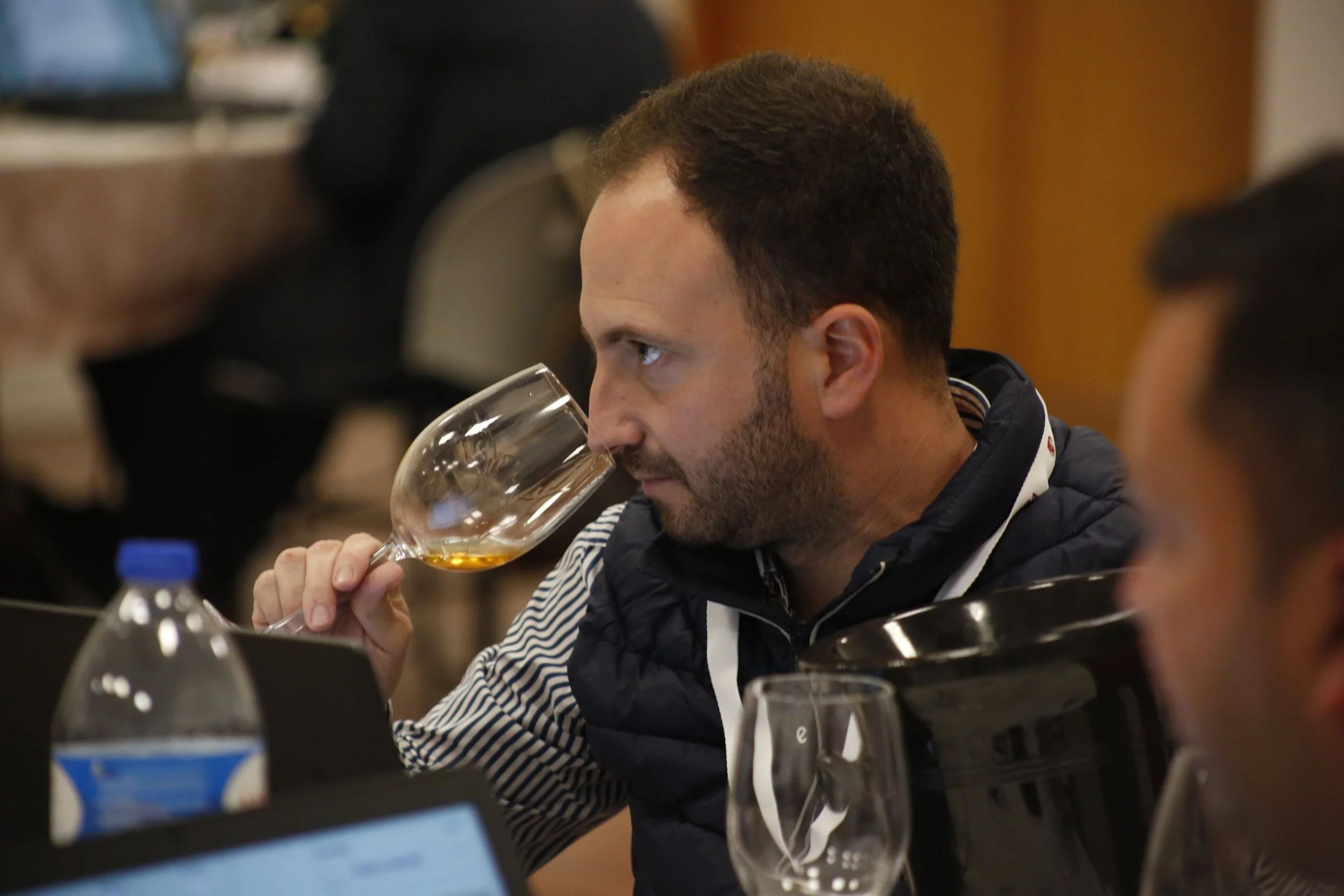Homem segurando taça de vinho, degustando em ambiente de conferência ou evento.