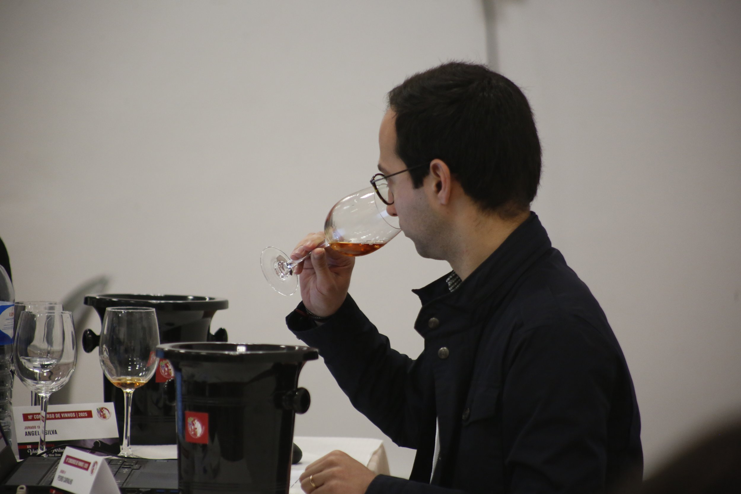 Homem apreciando taça de vinho escuro em evento de degustação.
