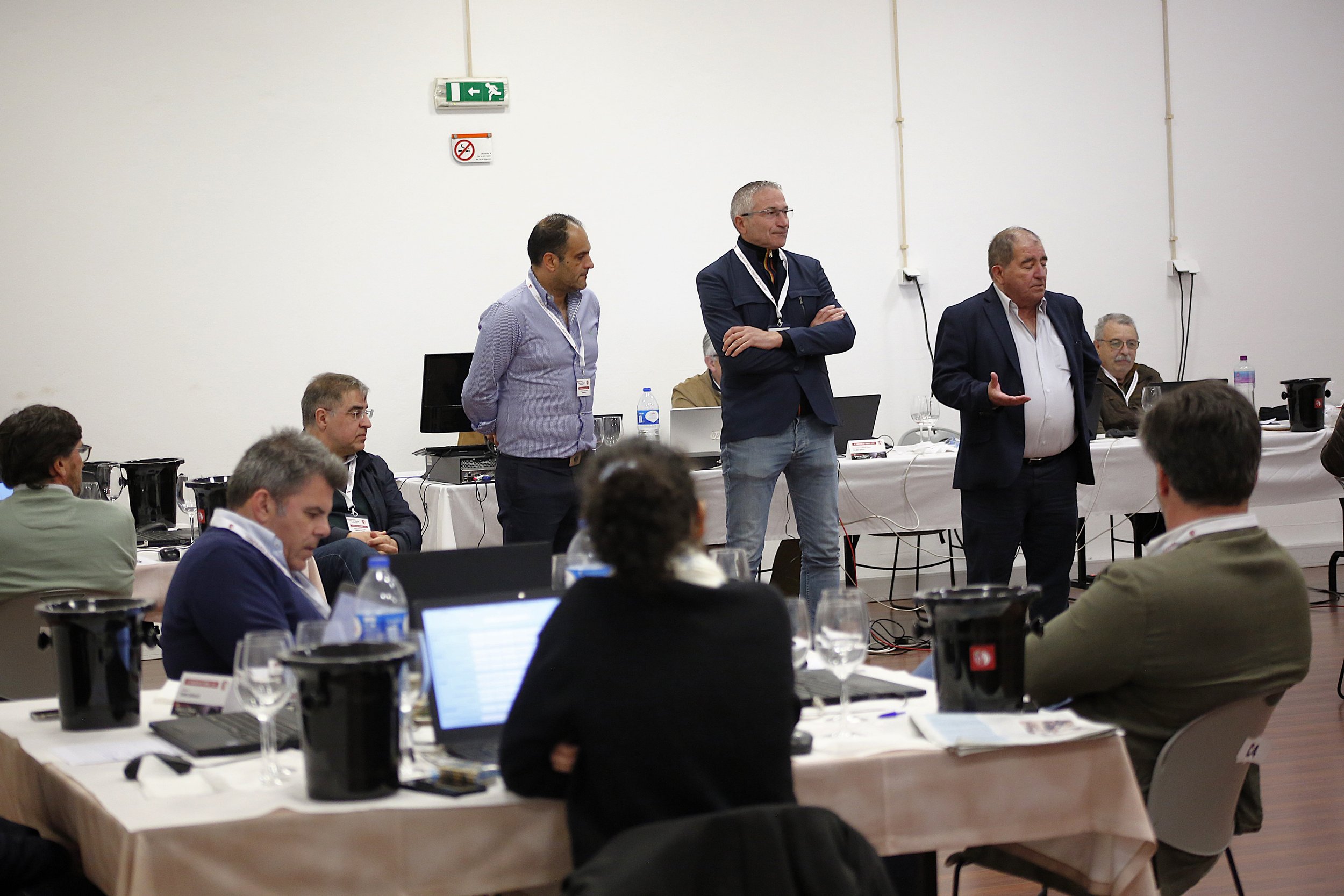 Reunião de negócios com vários participantes, alguns sentados e outros em pé, na sala.