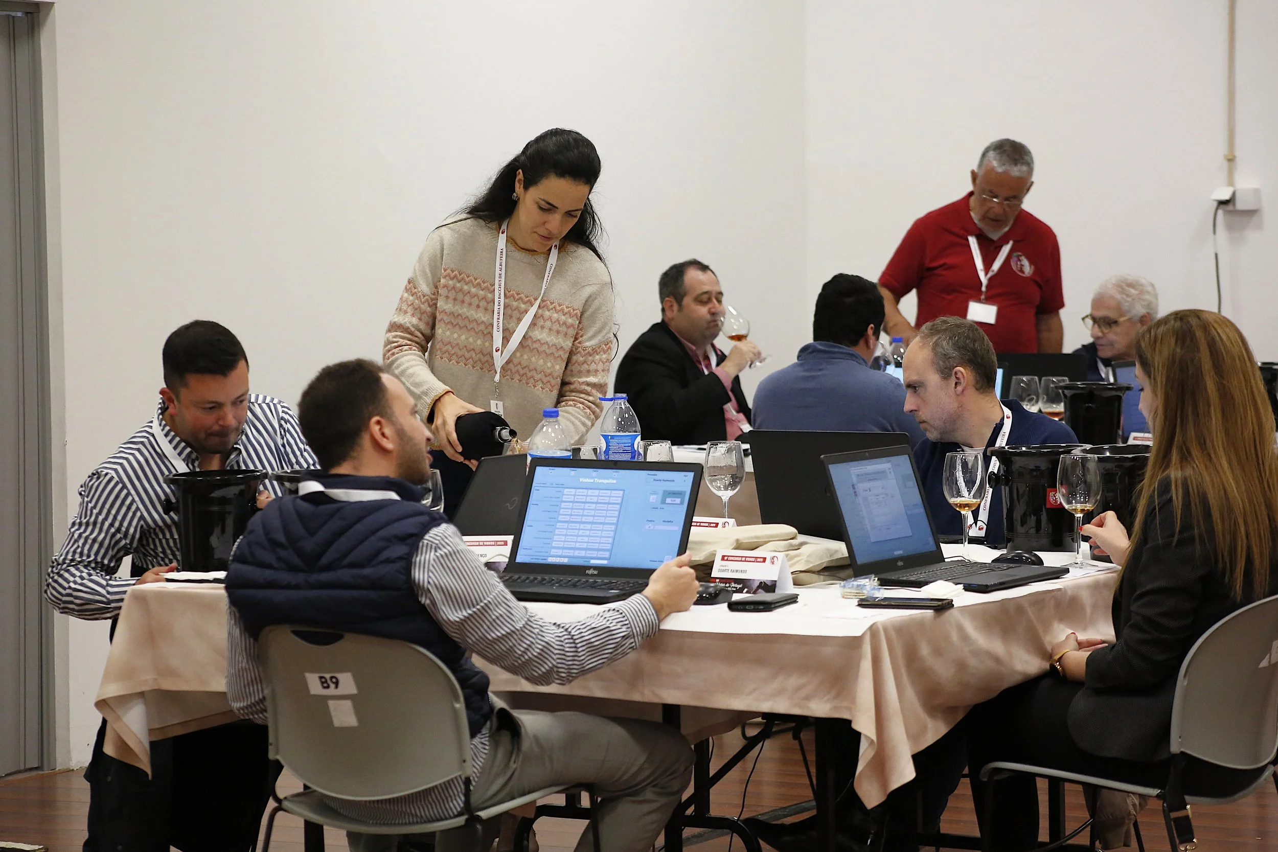 Reunião de negócios com várias pessoas usando laptops, alguns bebendo vinho, em uma sala de conferências.