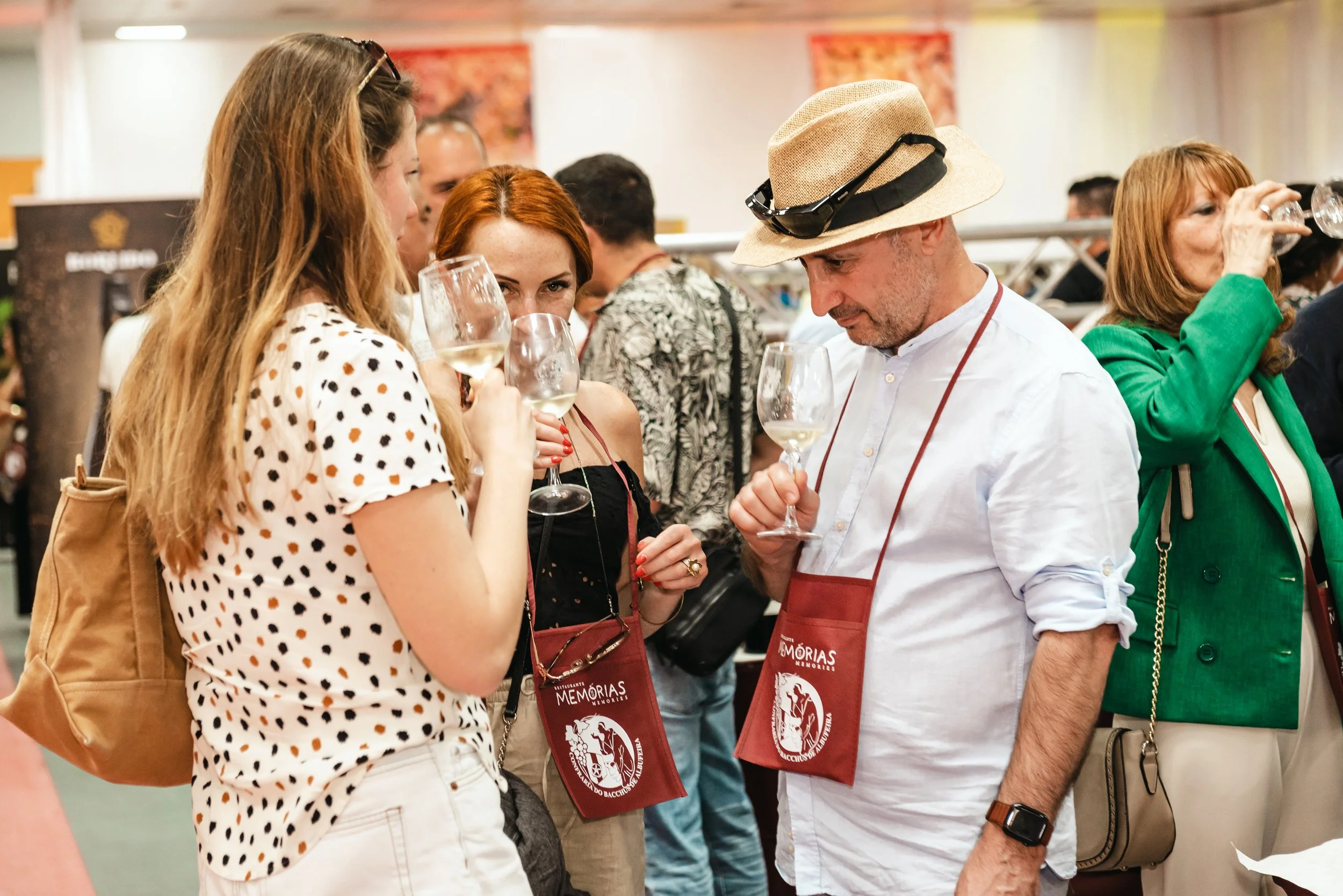 Grupo de pessoas degustando vinho em evento. Pessoas segurando taças de vinho e usando aventais com logotipo do evento.