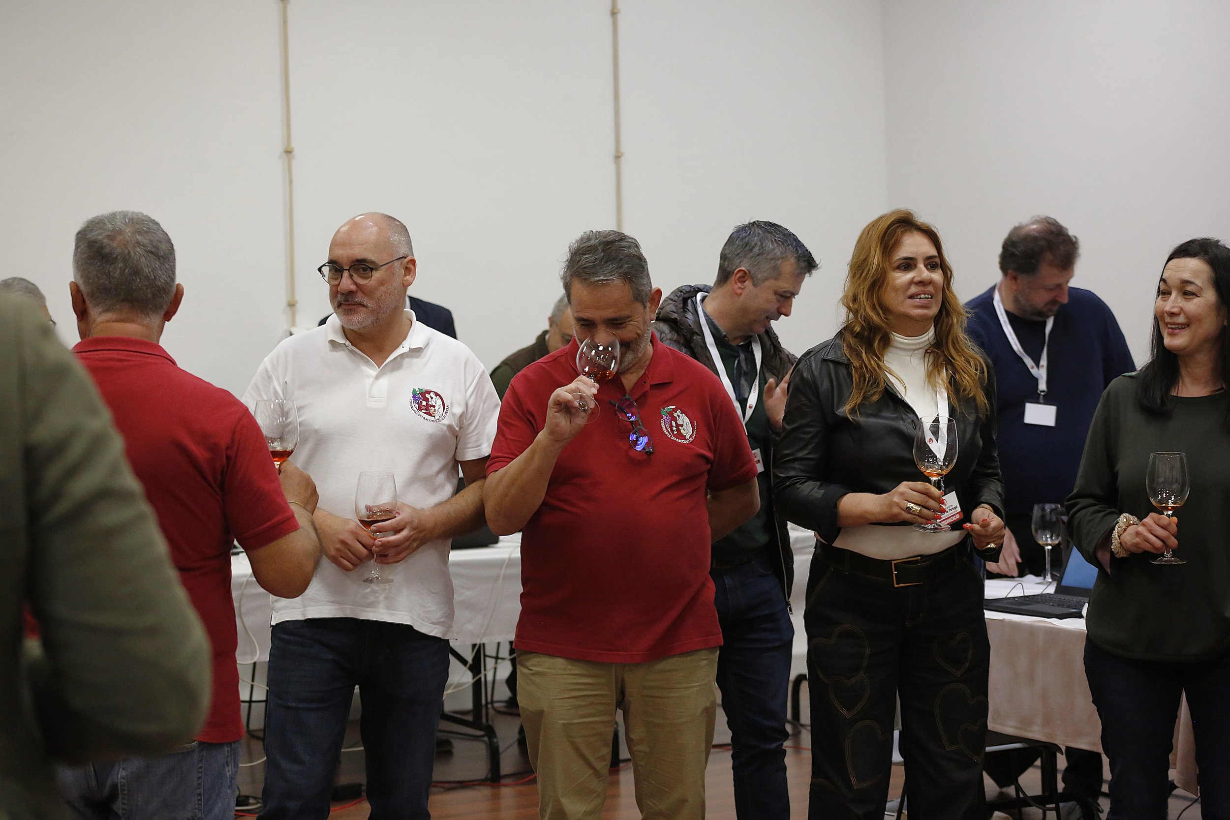 Grupo de pessoas em uma confraternização, segurando taças de vinho, dentro de uma sala com mesa e computador ao fundo.