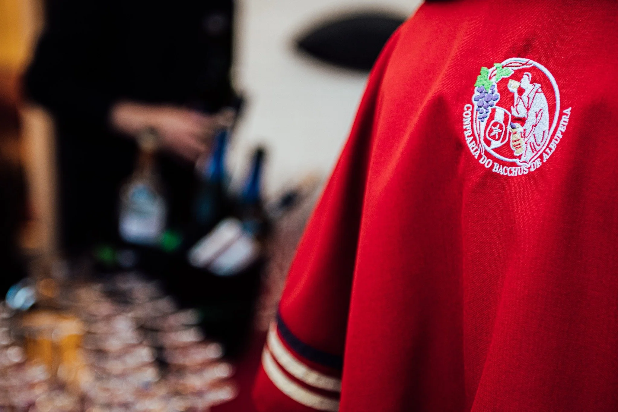 Close-up de uma camiseta vermelha com logotipo da Cooperativa do Bacchus de Alergência, detalhes das mangas com faixas brancas e pretas.