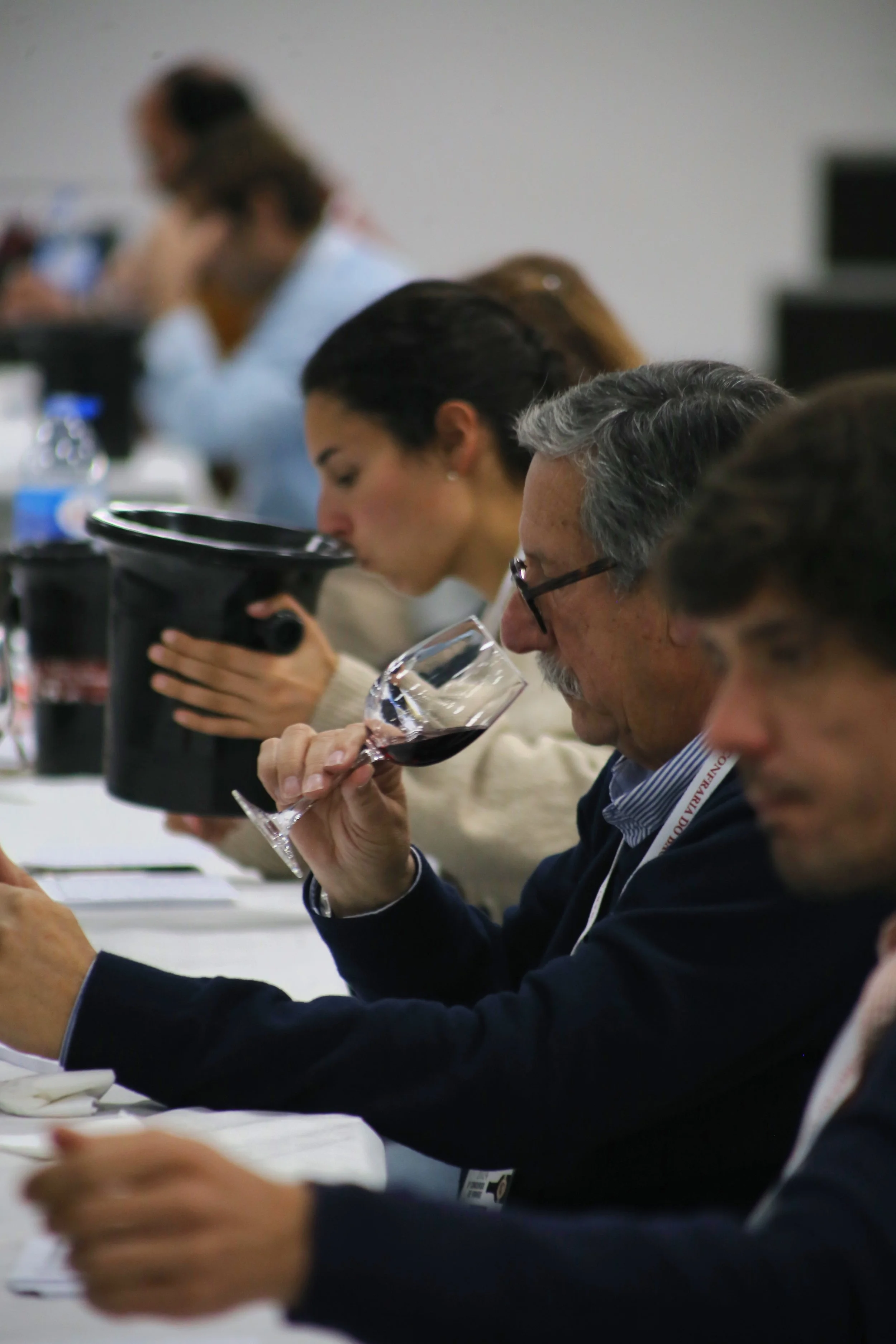 Pessoas em uma sala de reunião provando vinho, com uma pessoa segurando uma taça de vinho tinto na mão.
