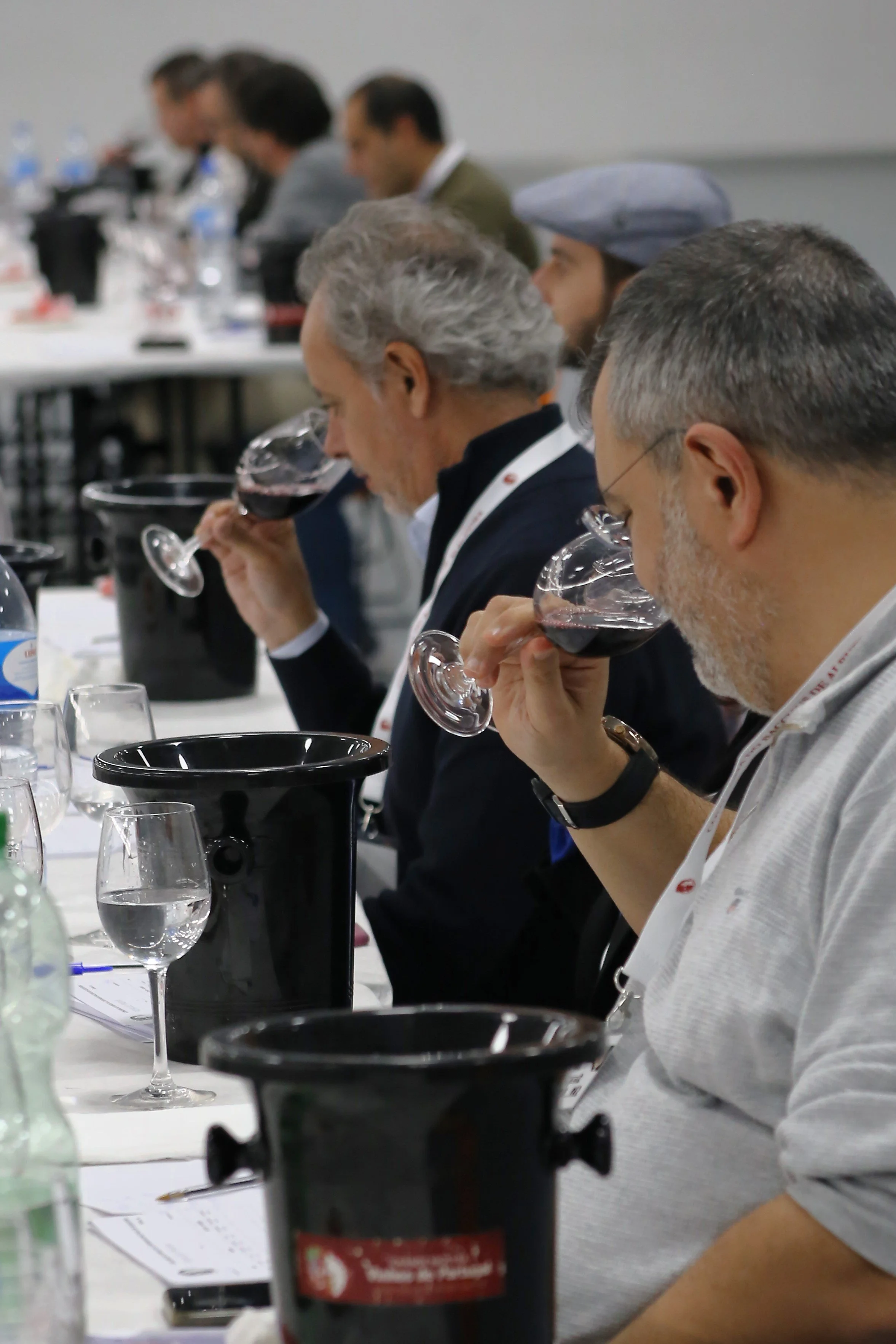 Homens em uma degustação de vinhos, usando taças e conzinhando em uma mesa com garrafas de água e utensílios