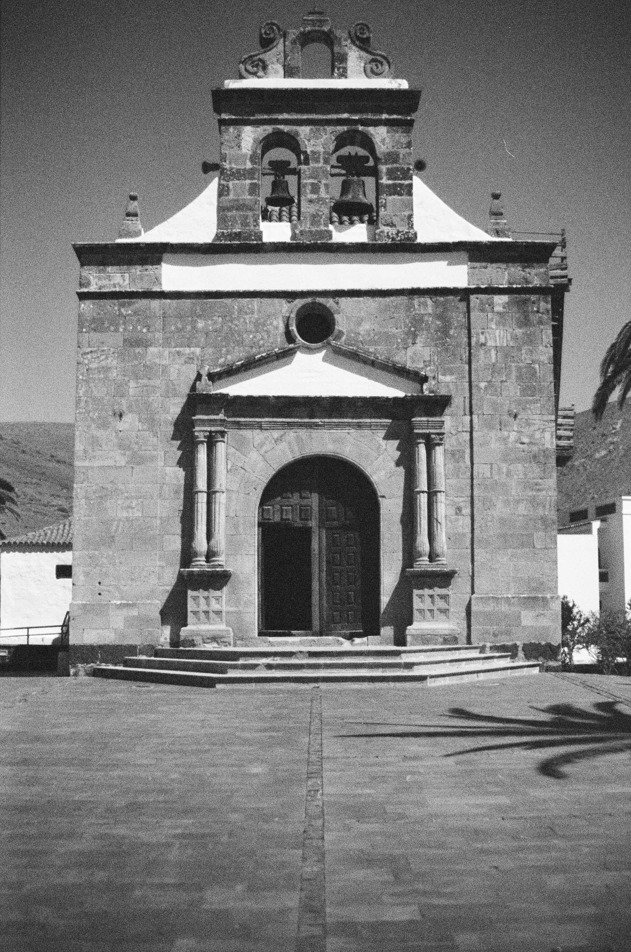 Black and white photo of a historic church or mission building with a bell tower, arched doorway, and steps leading up to the entrance.