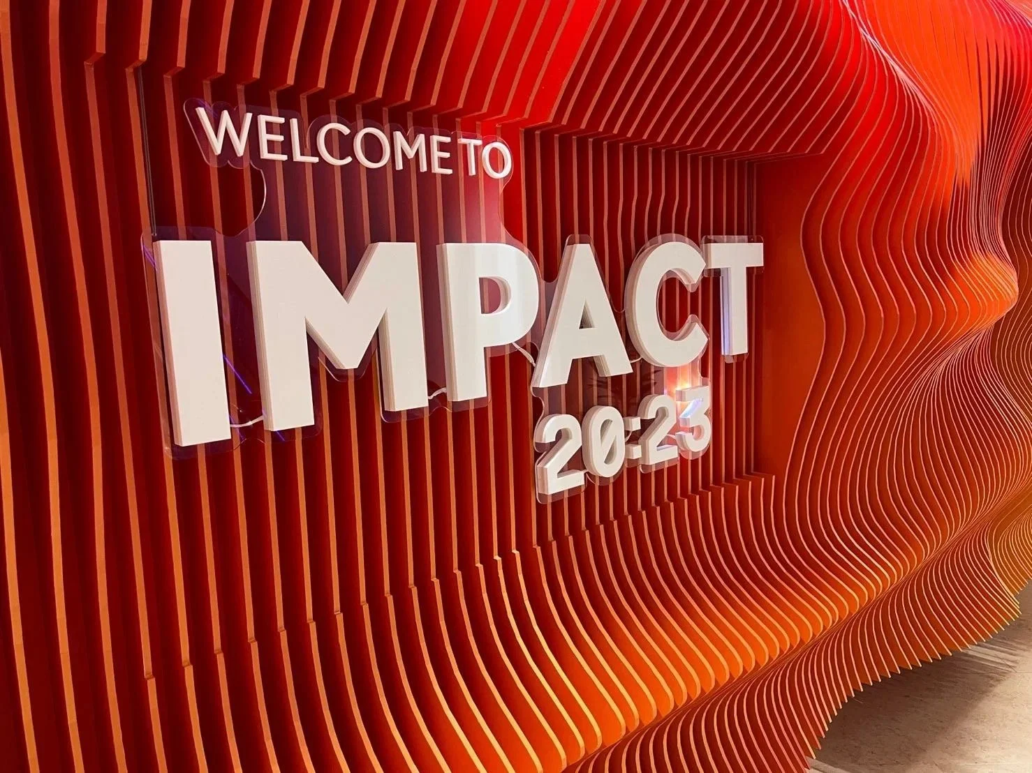 Photo of a modern, textured orange wall with a sign that reads "WELCOME TO IMPACT 20-23" in large 3D white letters.