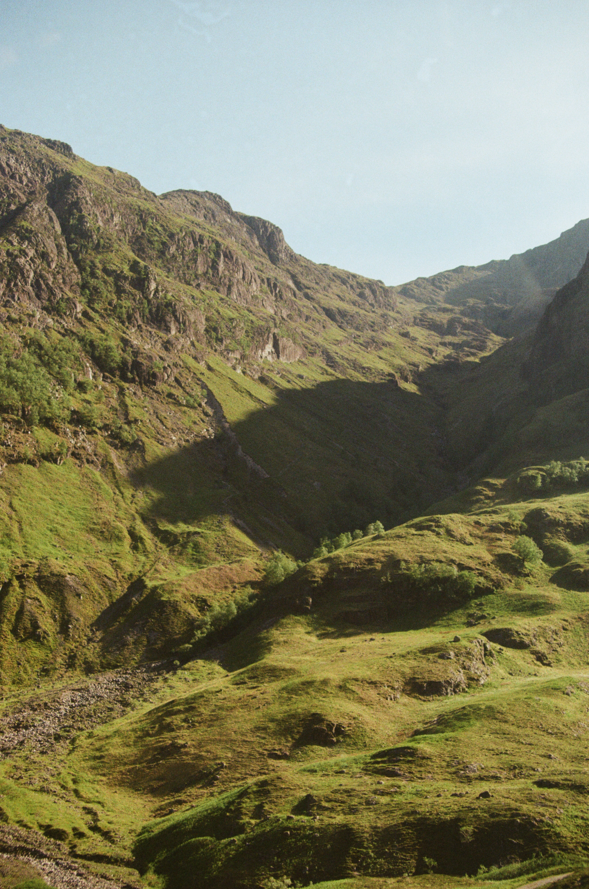 Scenic view of green rolling hills and rugged mountains under a clear sky.