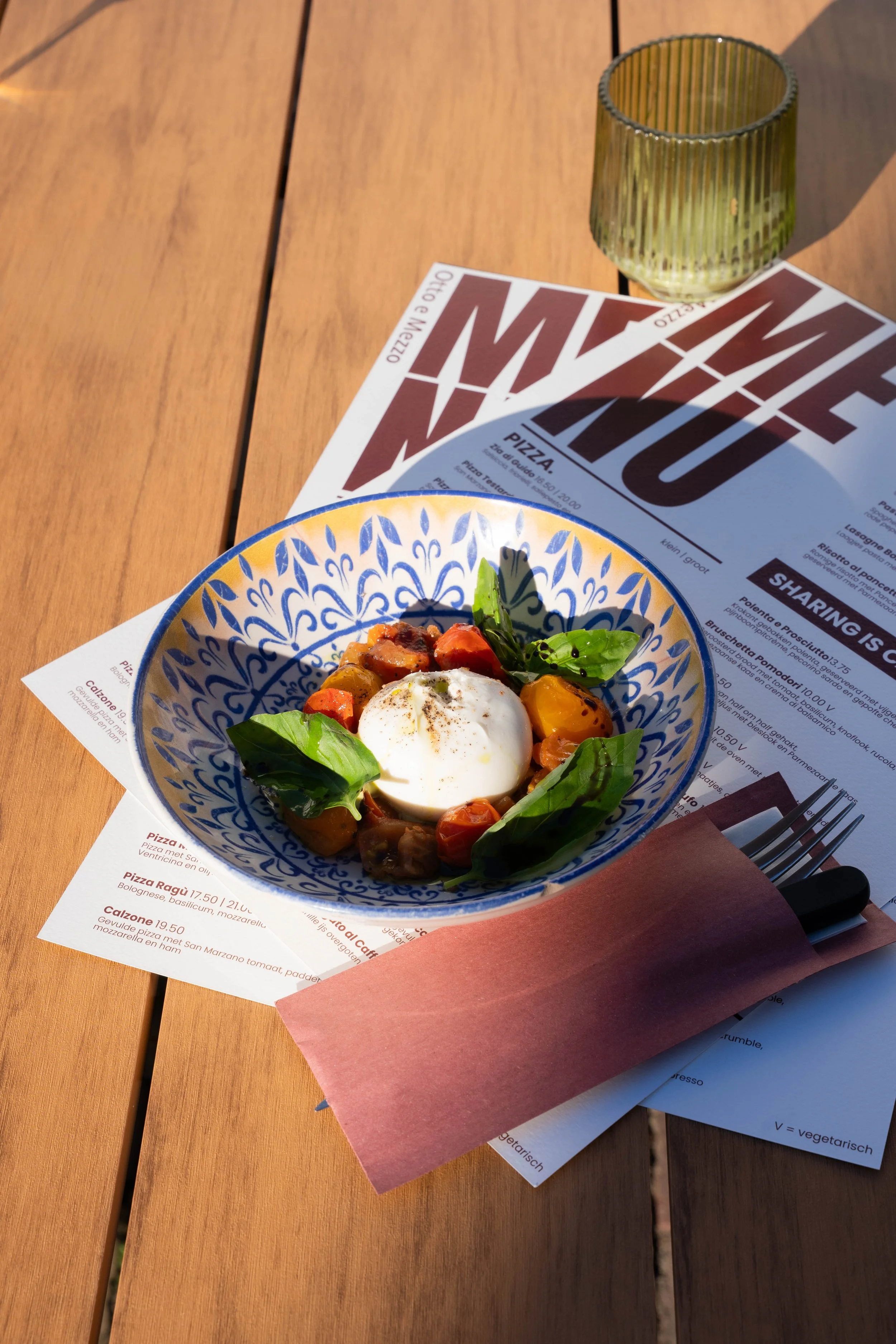 A wooden table with a menu, a glass, and a decorative bowl of food topped with herbs and a poached egg.