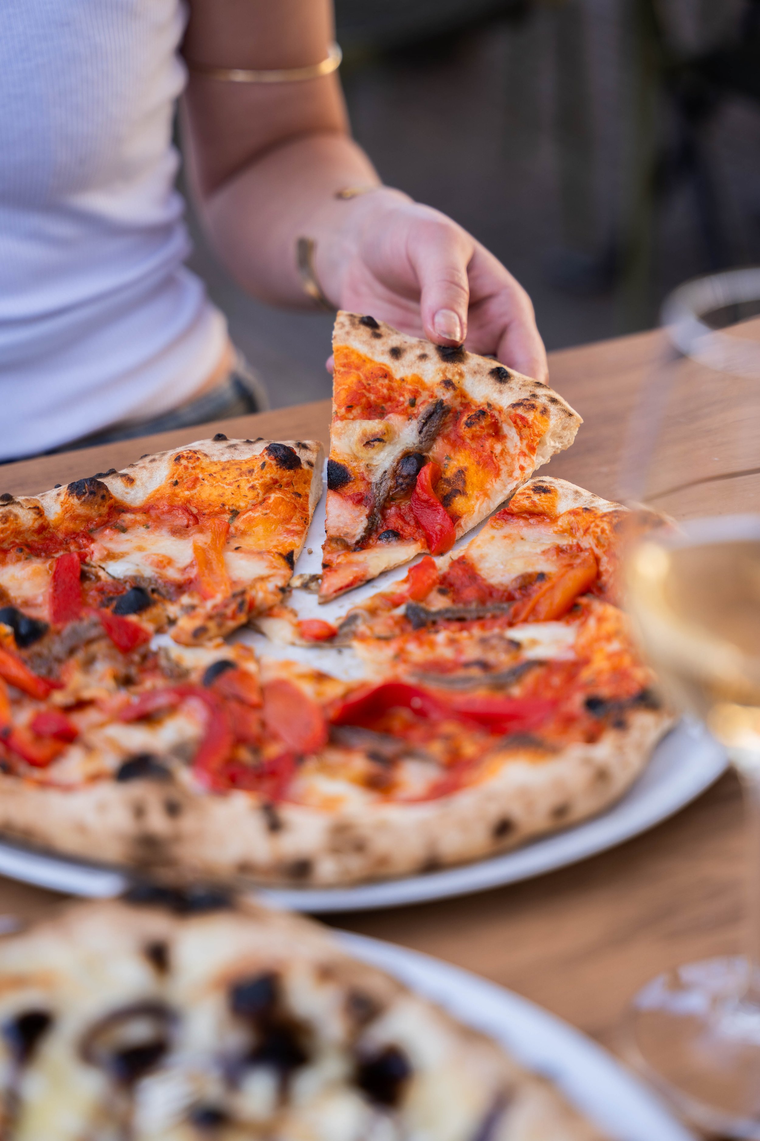 Close-up of a person picking up a slice of pizza with pepperoni, peppers, and mushrooms from a pizza tray