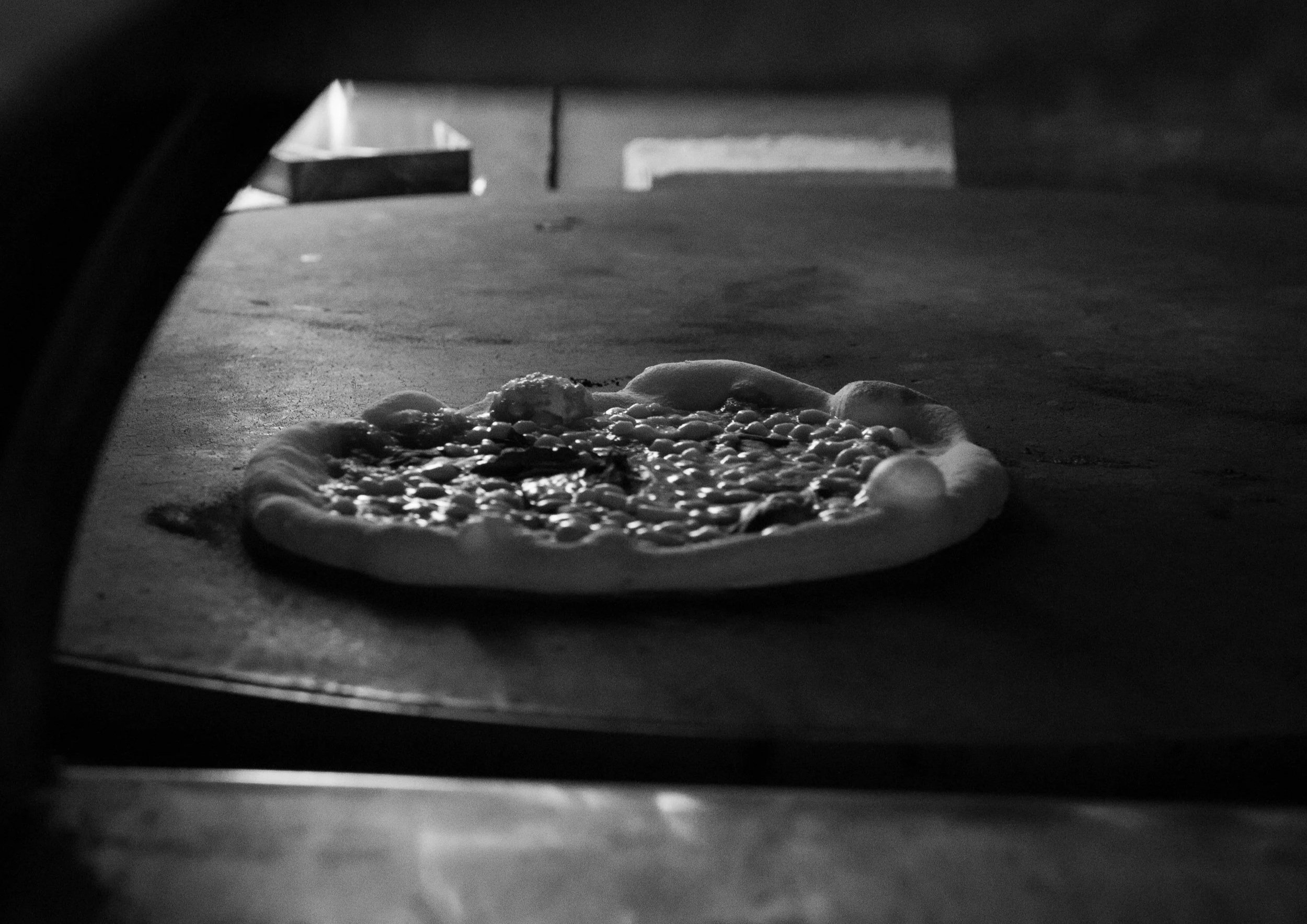 A pizza baking in a pizza oven viewed from underneath, with the pizza crust and toppings visible.