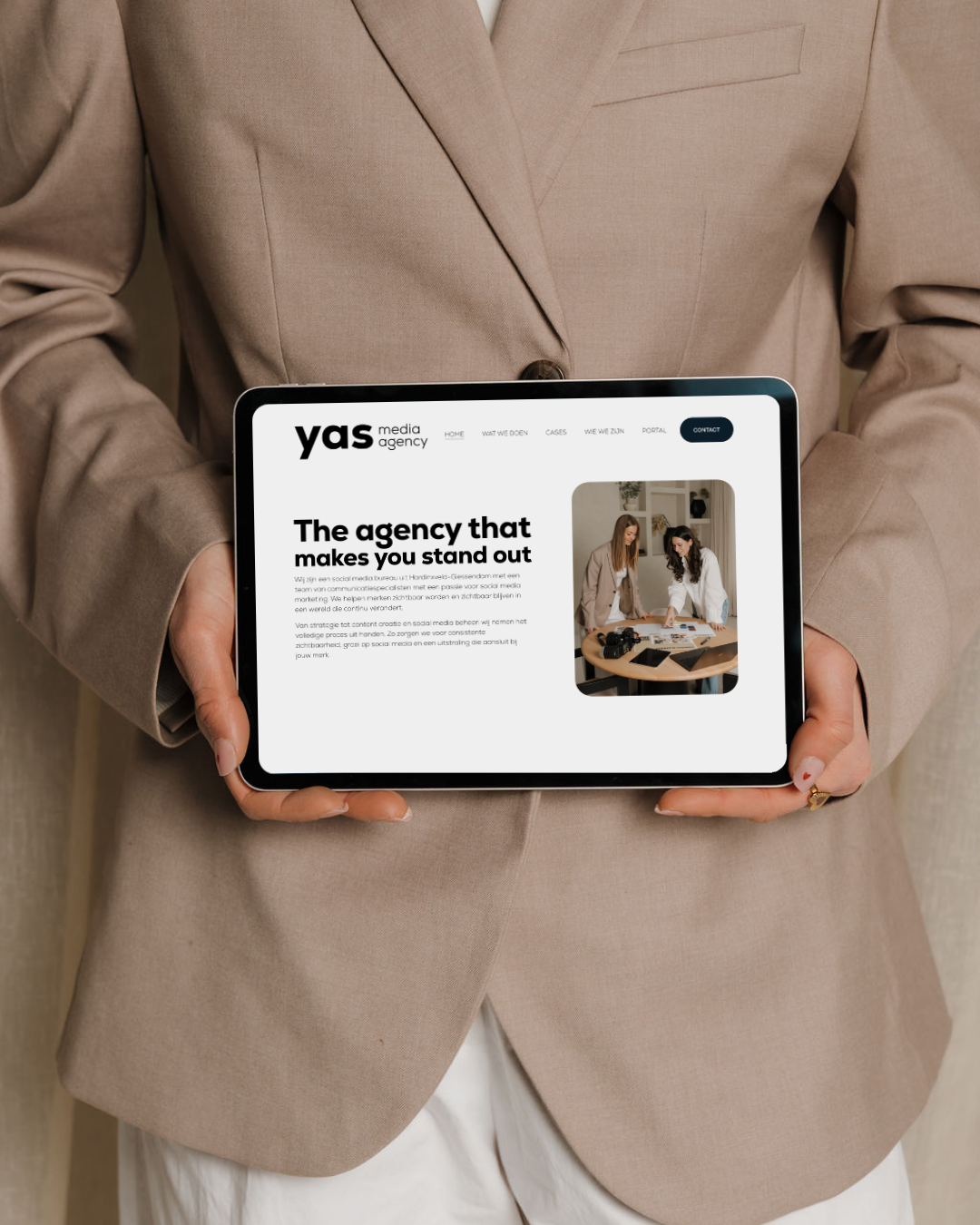 Een persoon in een beige pak houdt een tablet met de website van een mediabureau, YAS media agency, zichtbaar.