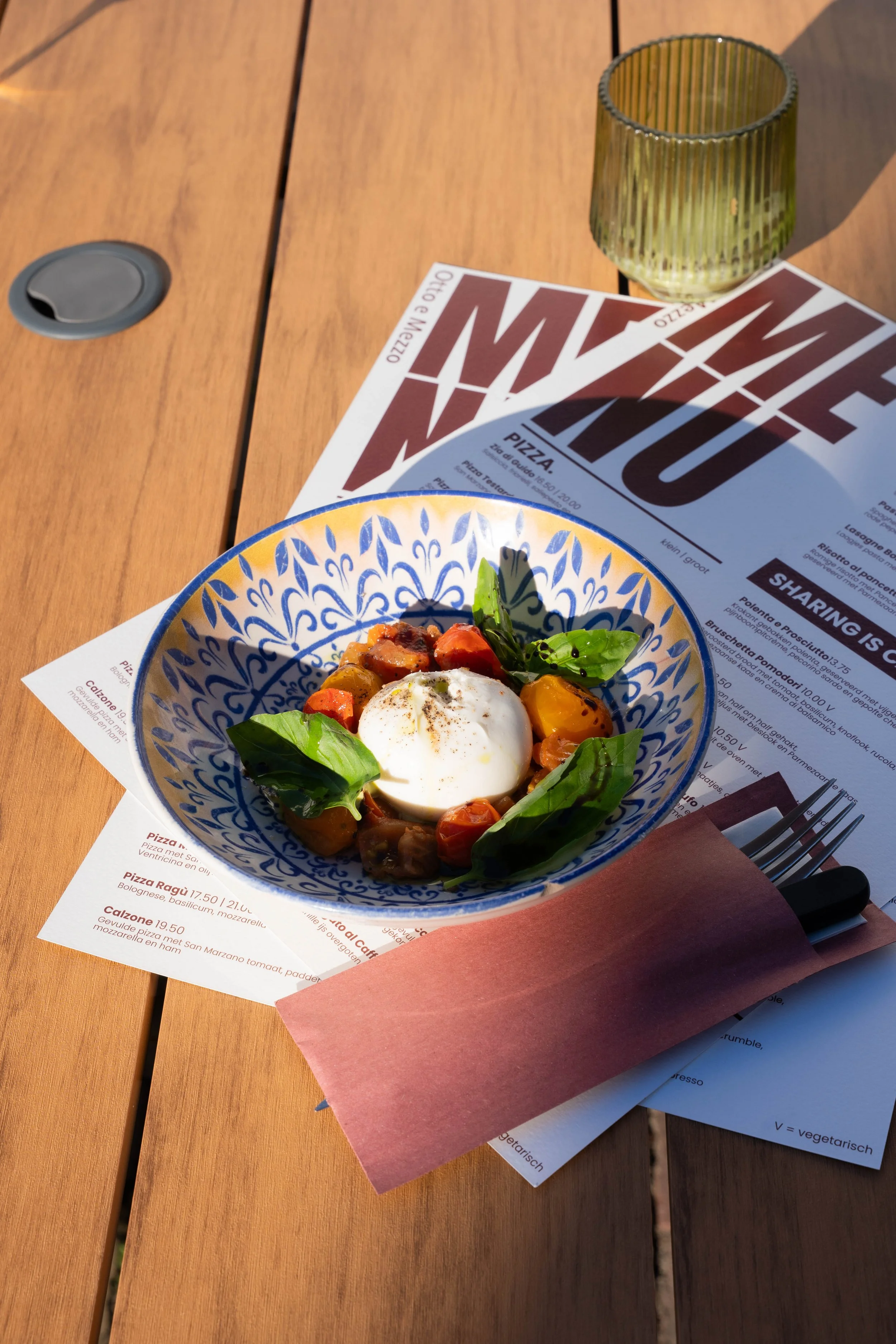 A wooden table with a colorful bowl of food, a glass, and a menu.