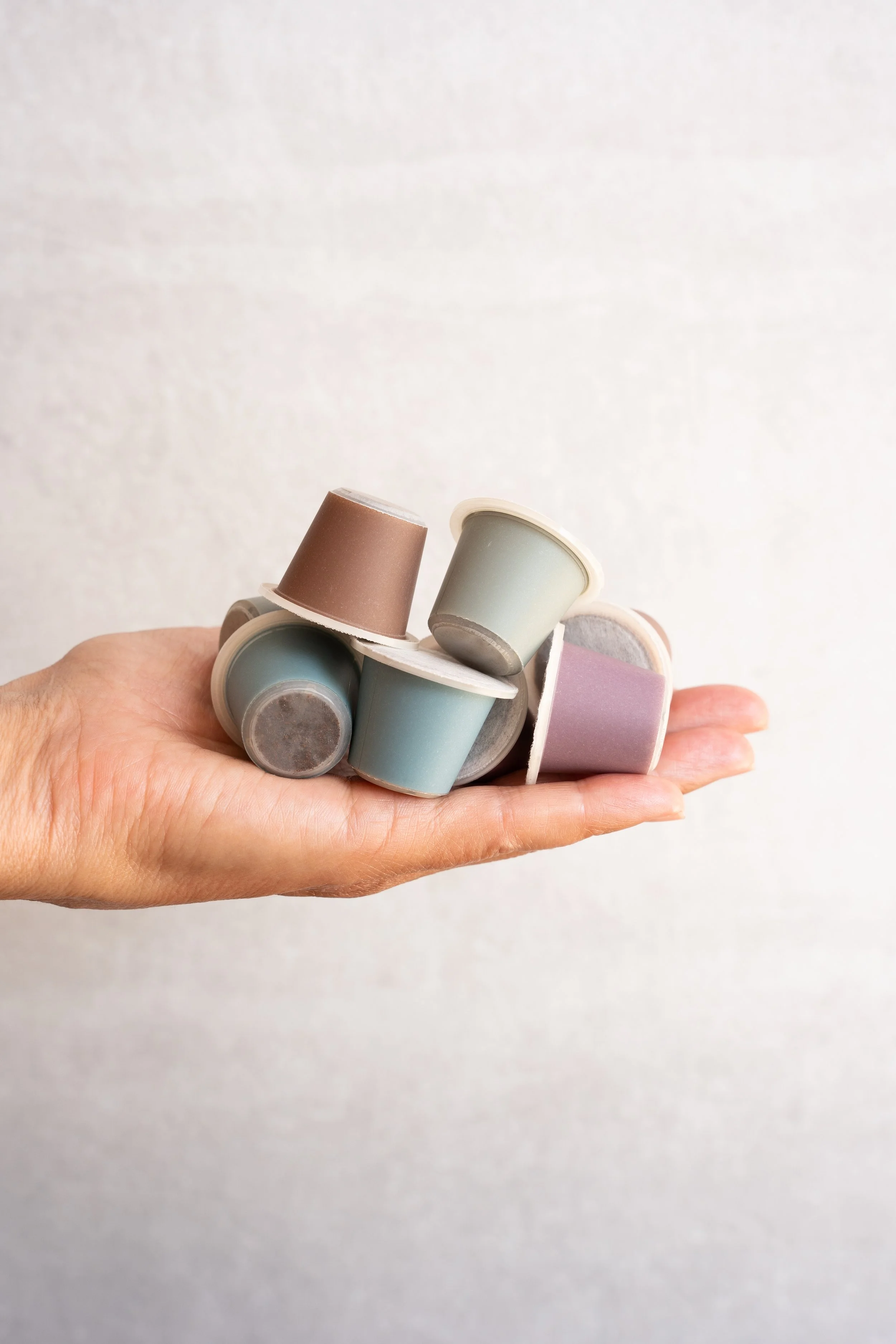 A hand holding several pastel-colored coffee capsules against a plain white background.