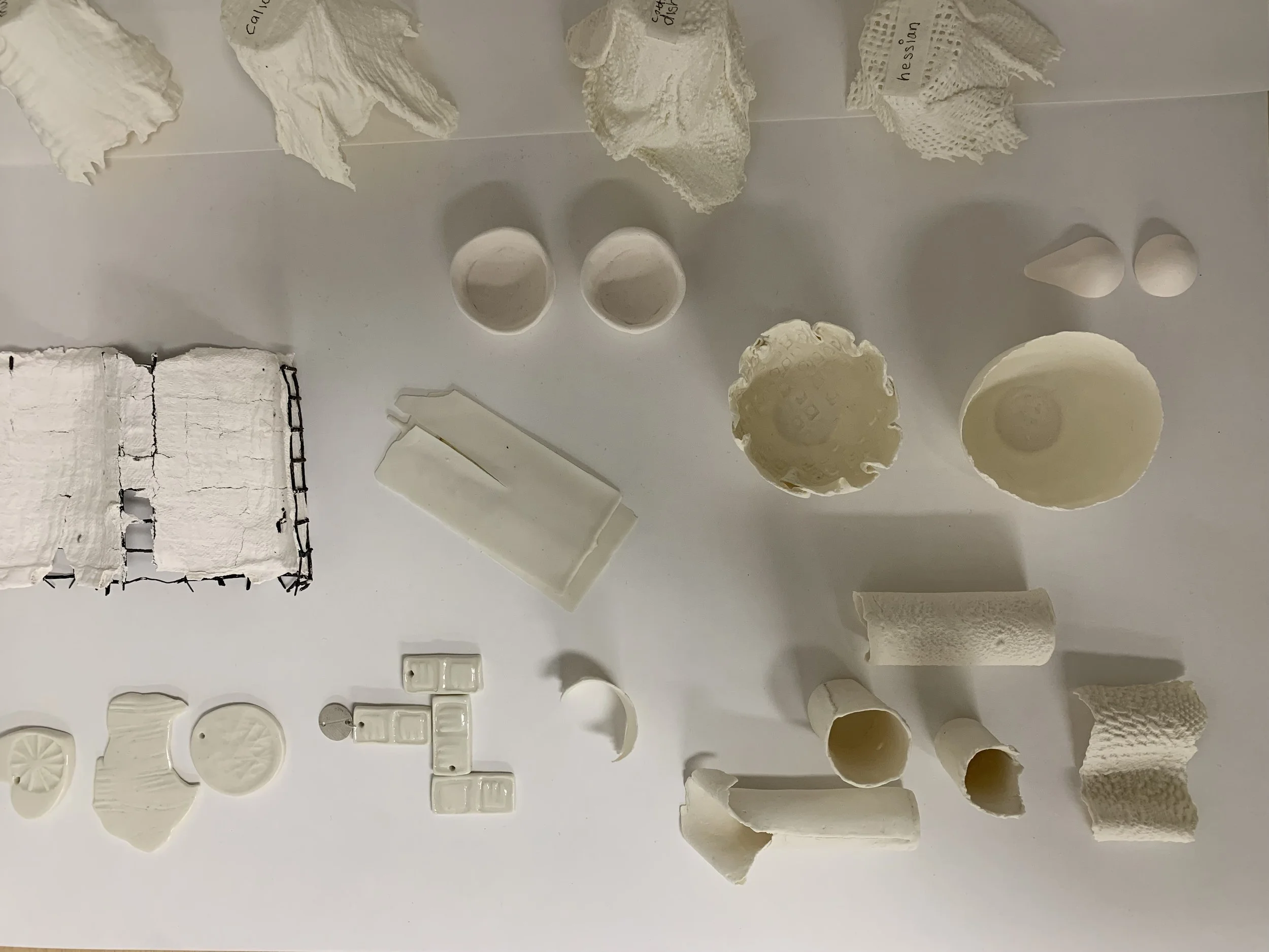 Various white ceramic and porcelain objects and fragments, including bowls, plates, tiles, and decorative pieces, arranged on a white surface.