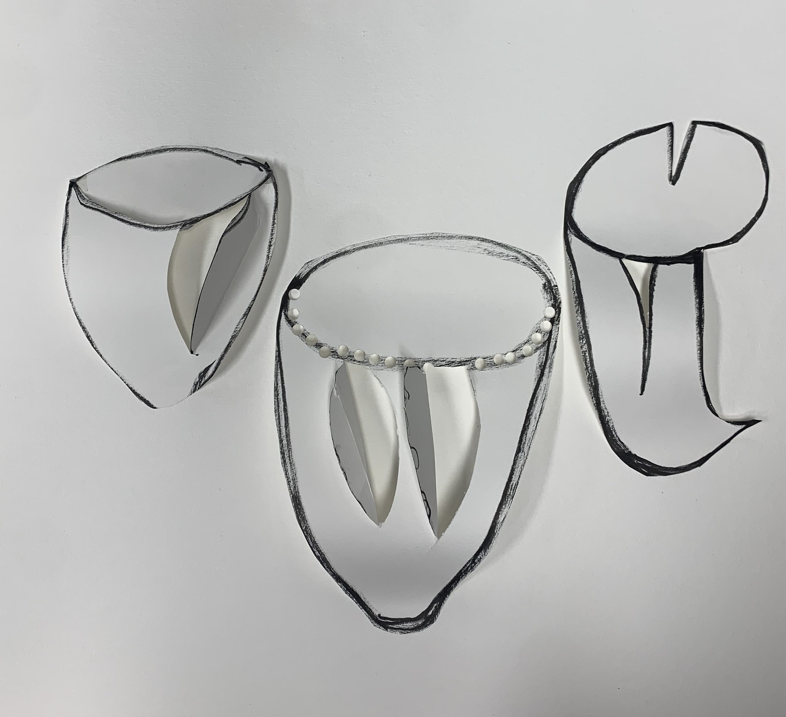 Hand-drawn sketches on white paper, with cut-out sections revealing 3D objects inside, and pearl-like beads decorating one of them.