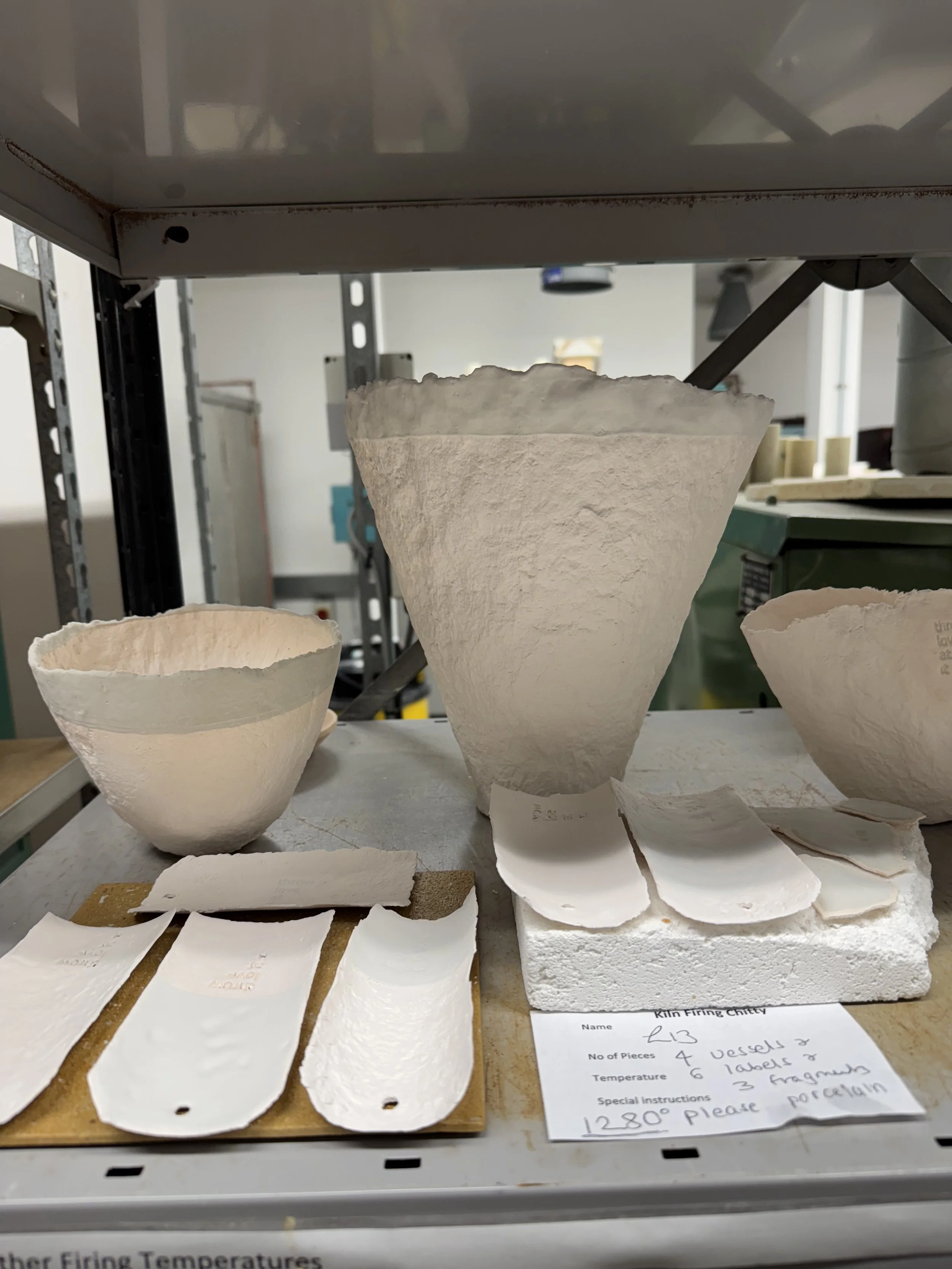 Porcelain pieces in various stages of formation on a kiln shelf in a pottery studio