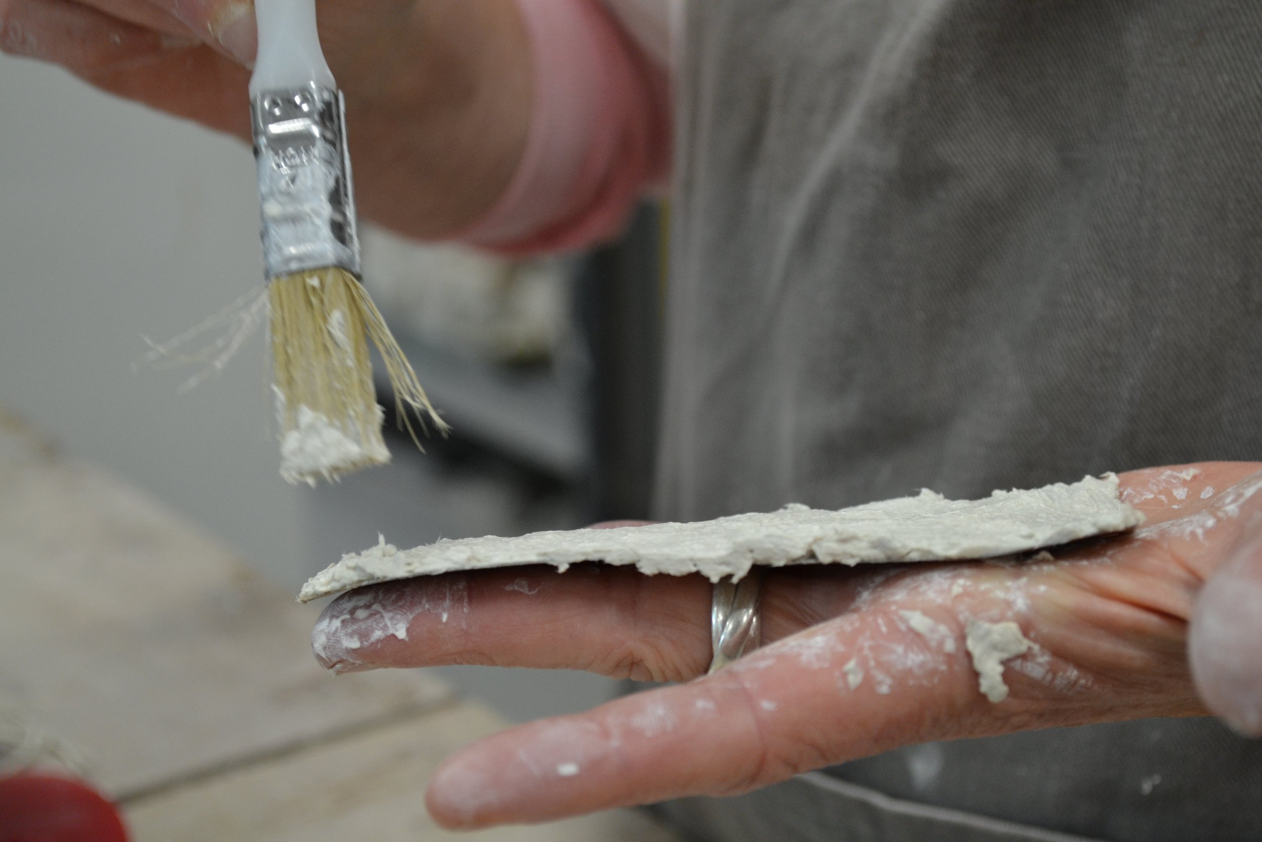 Person applying ceramic to a thin, rectangular piece of dough or bread with a small brush