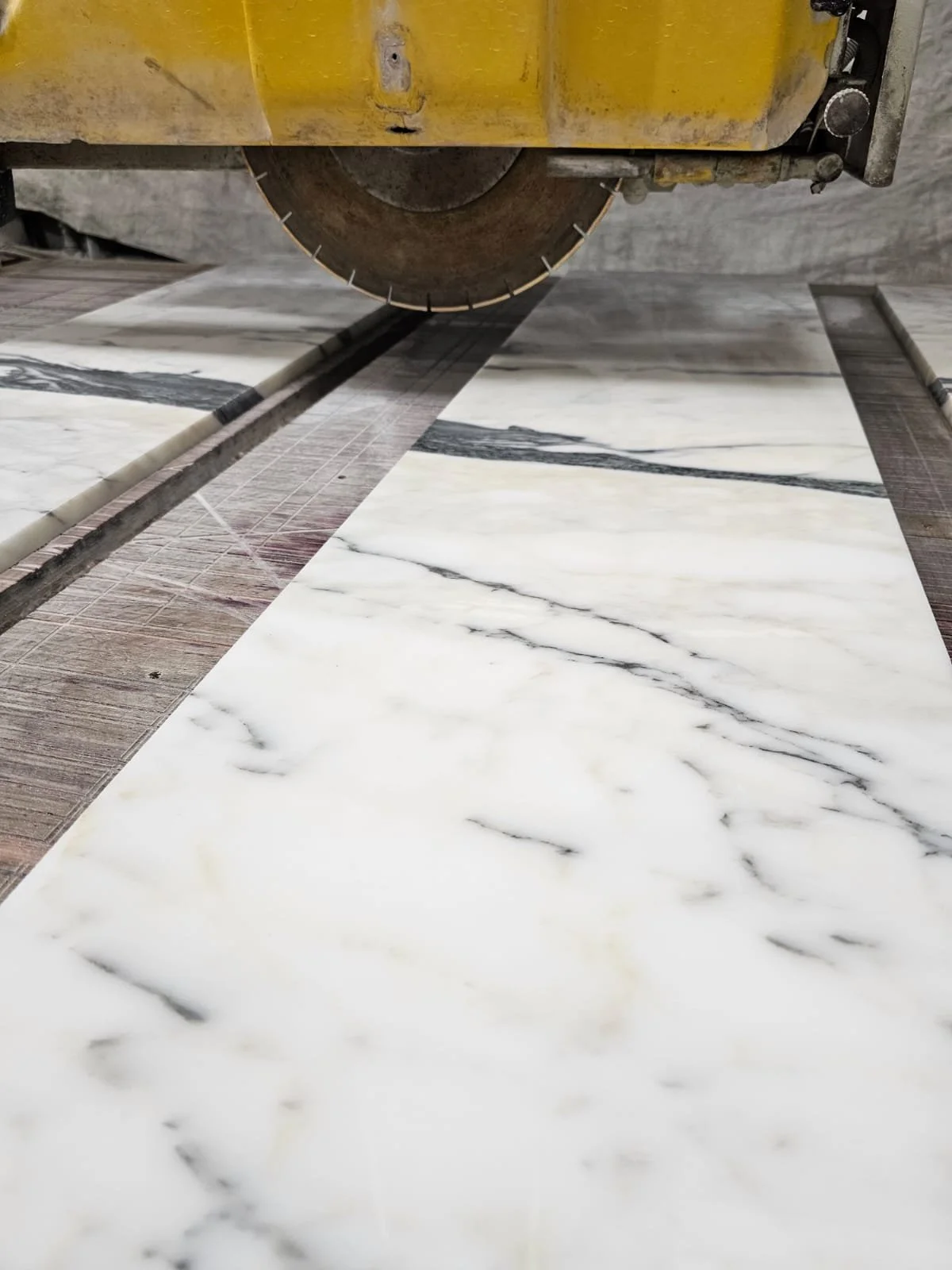 A marble saw cutting white marble tiles with black veining.