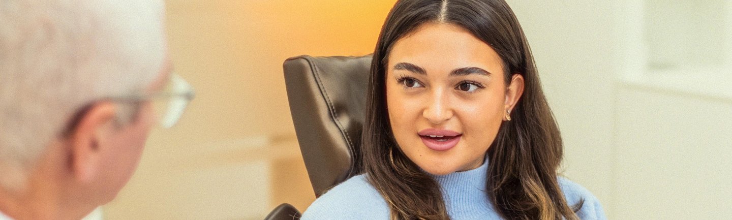 Junge Patientin im Gespräch mit einem Zahnarzt in einer modernen Praxis über ganzheitliche Zahnmedizin. Beratung zu Zusammenhängen zwischen Mundgesundheit und Allgemeingesundheit.