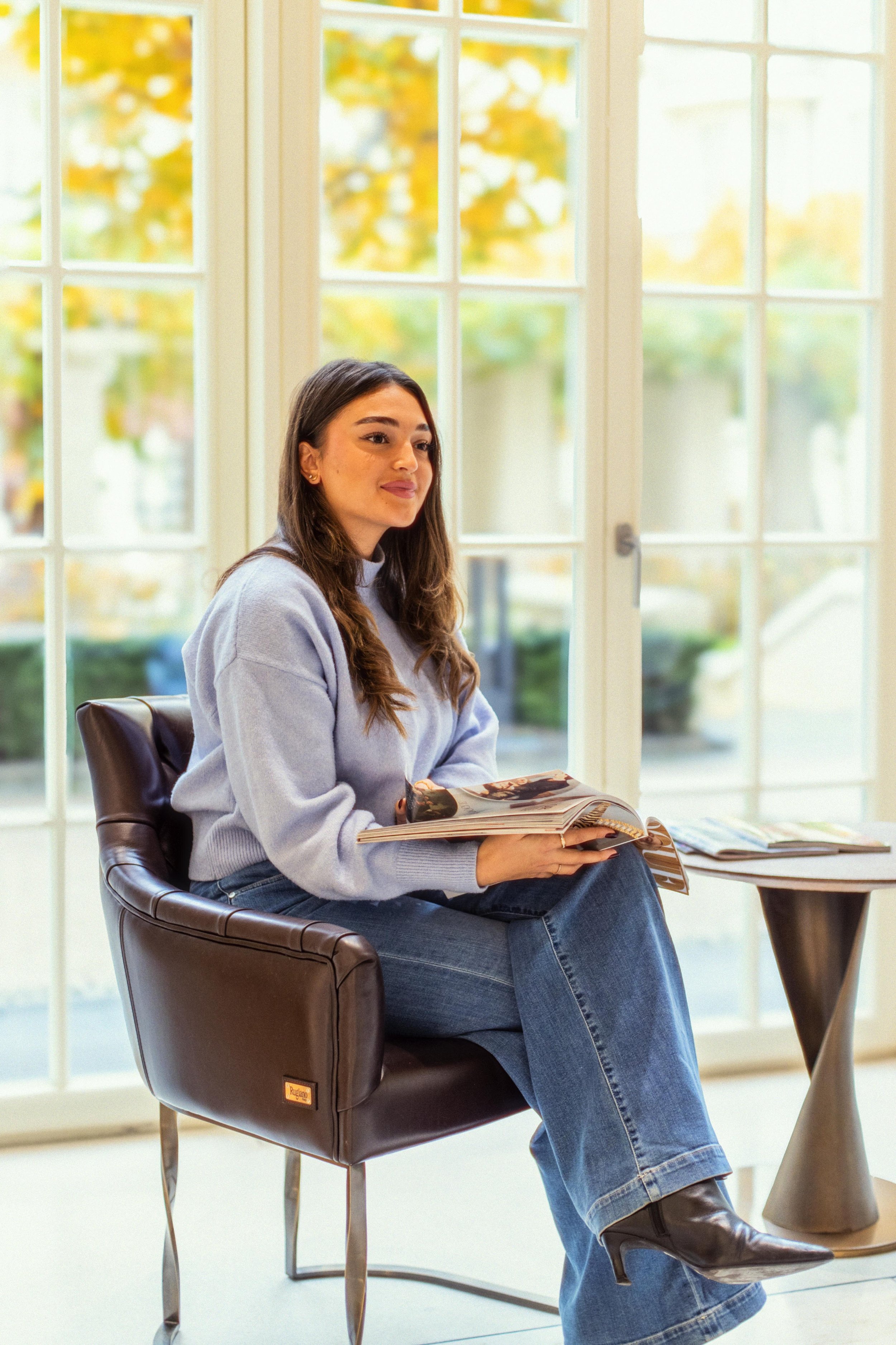 Junge Frau liest in einem Magazin in einer modernen, luxuriösen Zahnarztpraxis mit großen Fenstern und Blick ins Grüne. Ruhige Atmosphäre im Wartebereich.