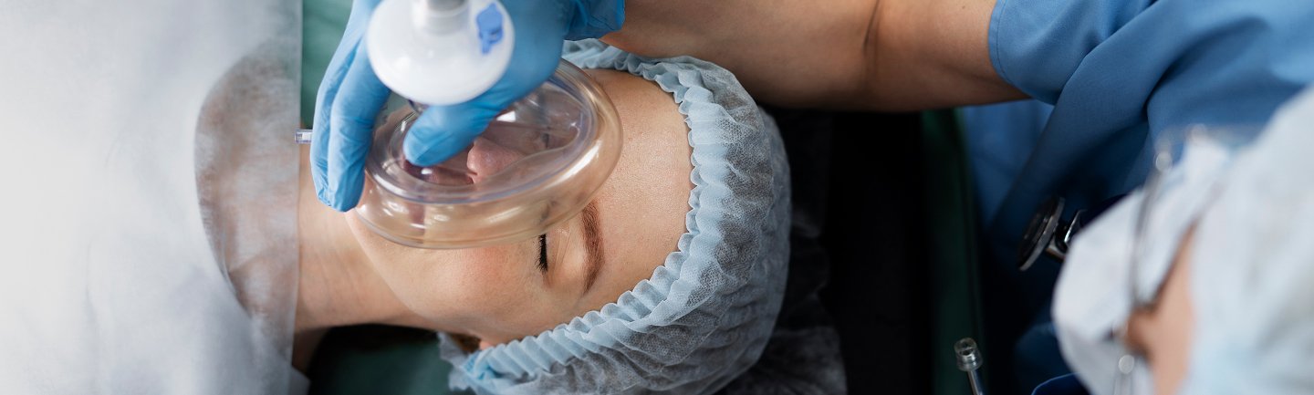 Patientin liegt unter Vollnarkose auf dem Behandlungsstuhl, Sauerstoffmaske wird zur allgemeinen Anästhesie angelegt