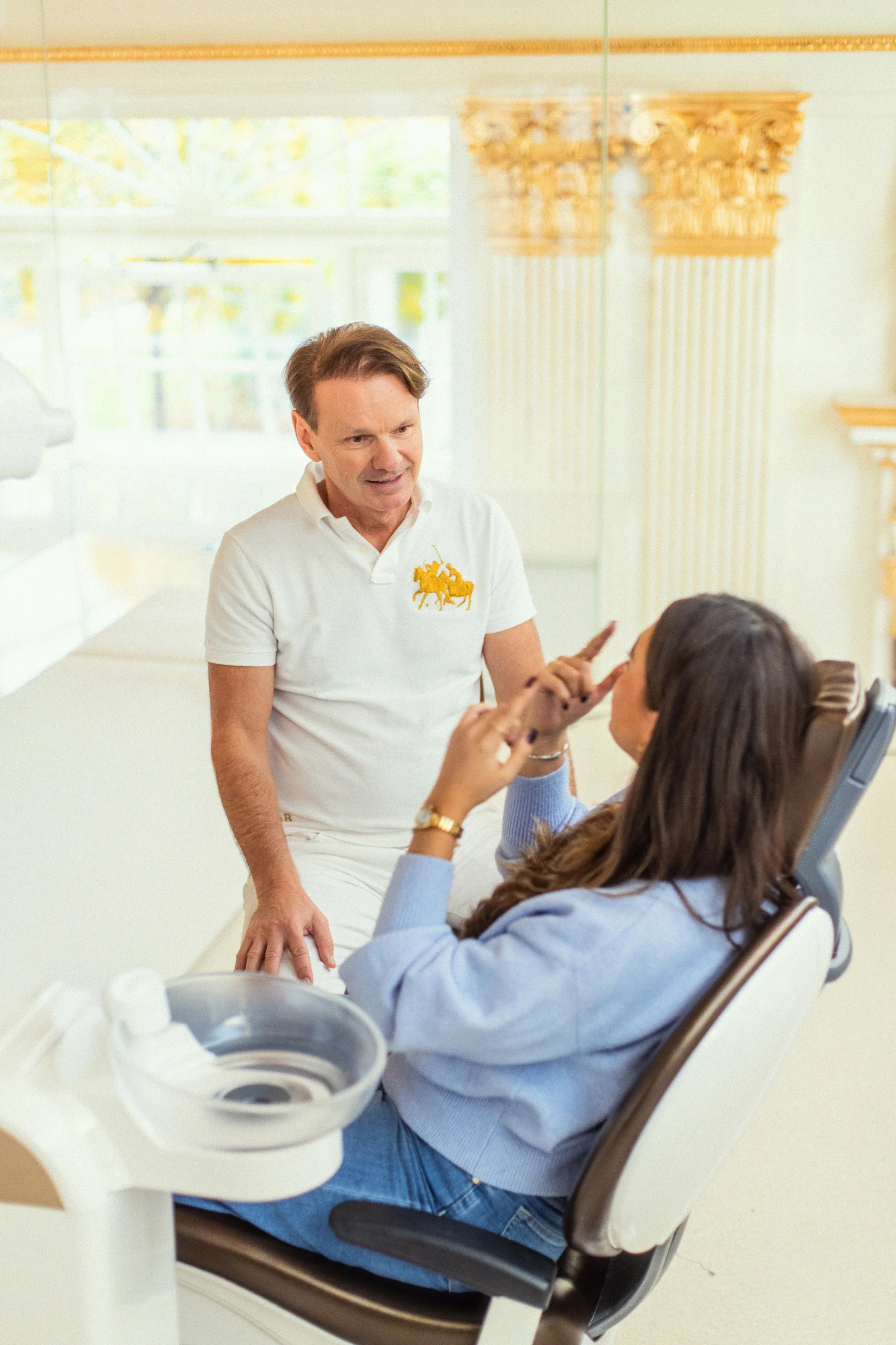 Zahnarzt und Patientin in einer hochwertigen, luxuriösen Zahnarztpraxis. Die Patientin sitzt im Behandlungsstuhl, während der Zahnarzt neben ihr steht und eine Behandlung sowie die weitere Patientenversorgung bespricht.