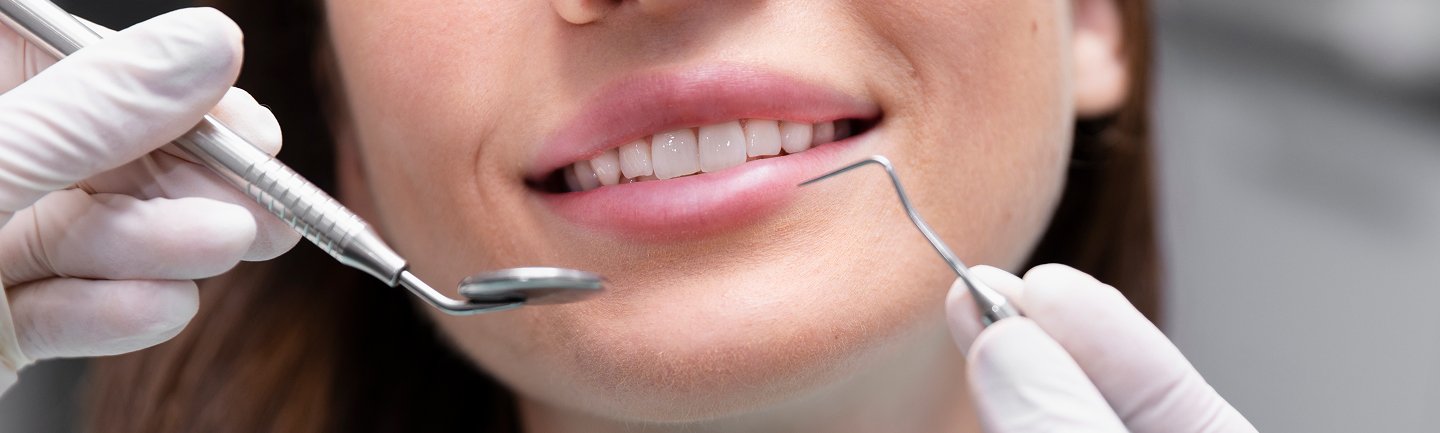 Nahaufnahme einer lächelnden Frau mit geöffnetem Mund, zahnmedizinische Instrumente bereiten die Behandlung vor