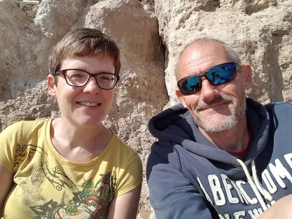 Helen and her partner Austin sittin in front of rock formations wearing sunglasses smiling into the camera