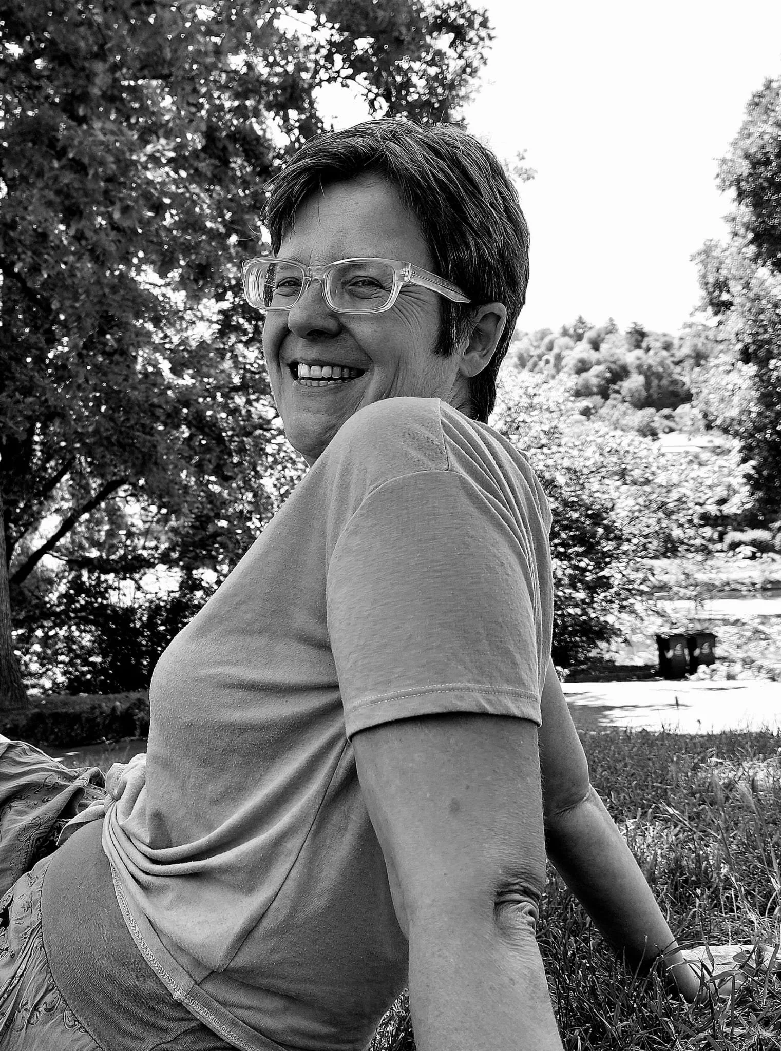 black and white picture of Helen the founder sat on grass amongst trees laughing
