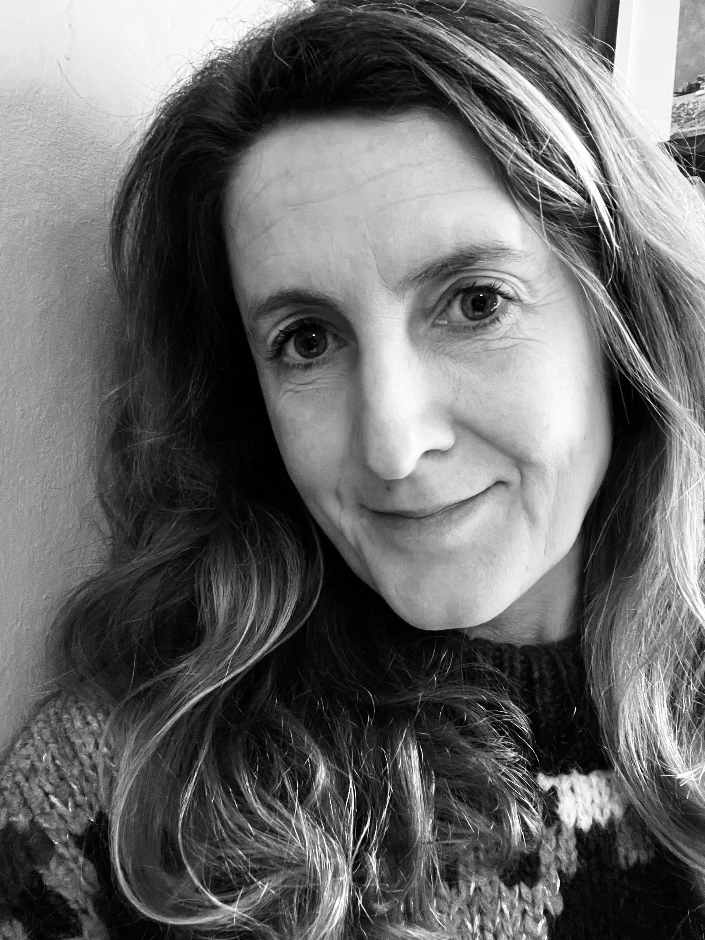Close-up black and white photo of a smiling woman with wavy hair, part of her face and hair visible.