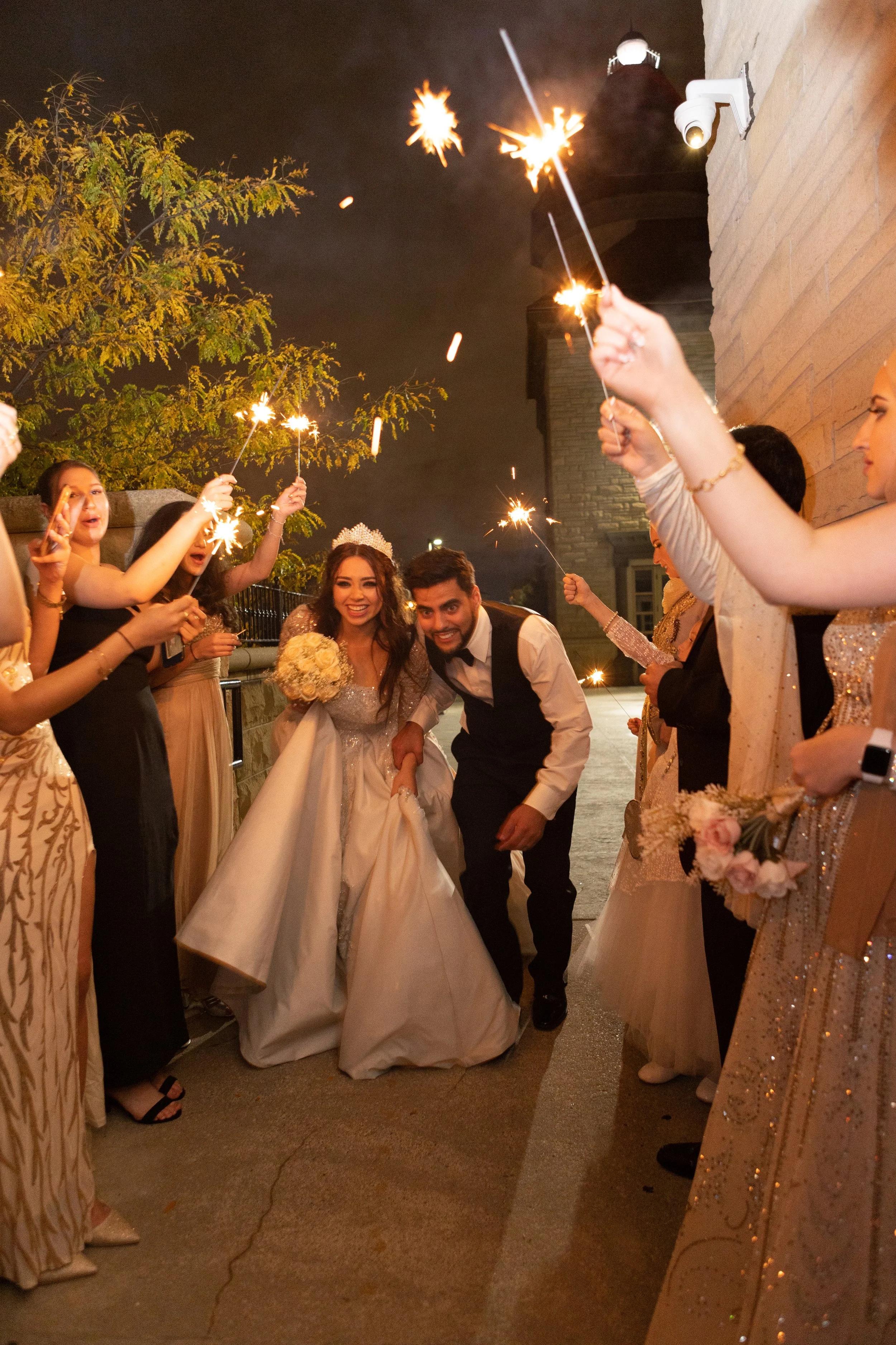 Bride and groom celebrating with friends holding sparklers at night outside.