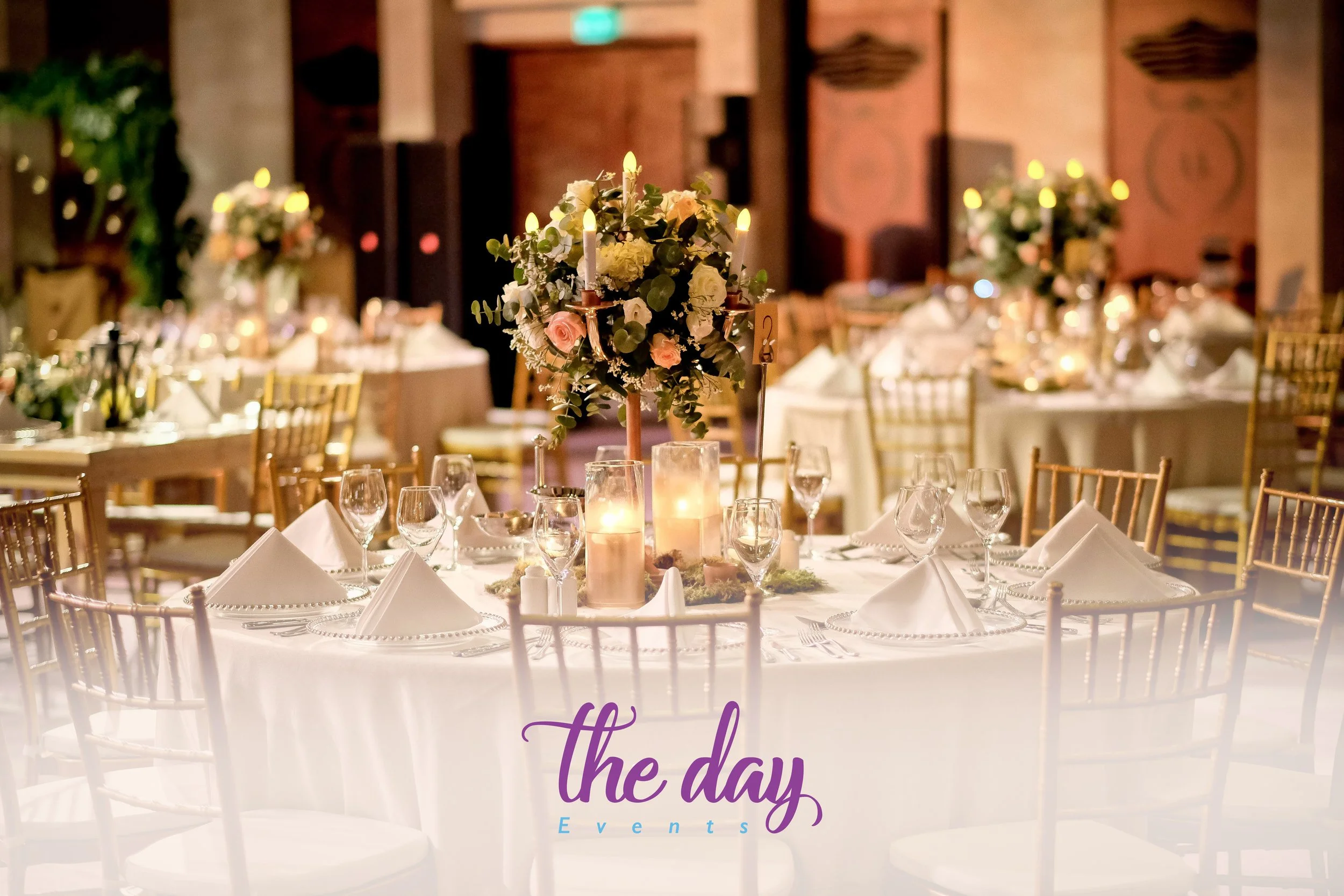 Elegant banquet table with white tablecloth, folded napkins, multiple wine glasses, floral centerpiece with candles, set for a formal event or wedding reception.