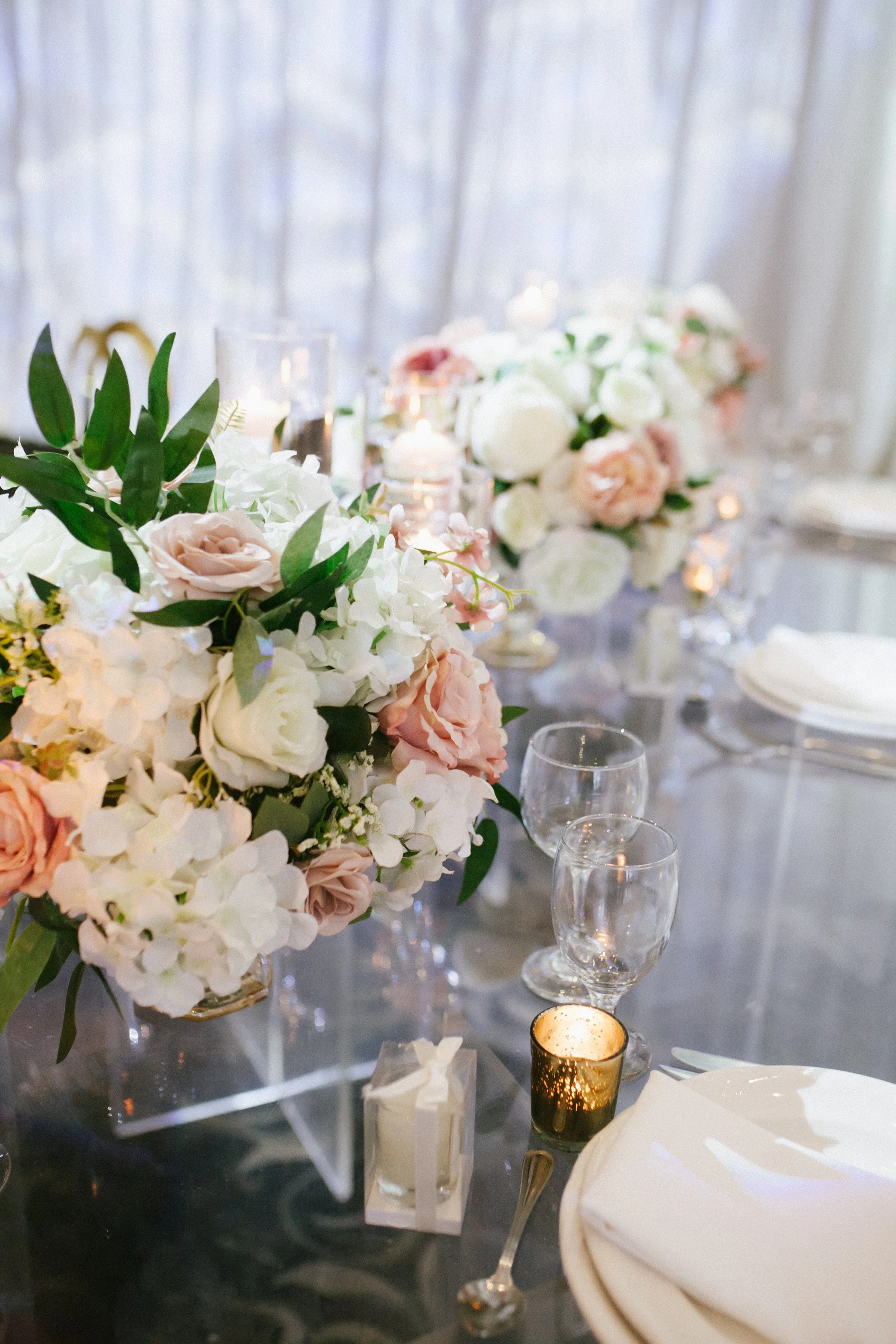 Elegant wedding reception table with floral centerpieces, candles, glassware, and place settings.