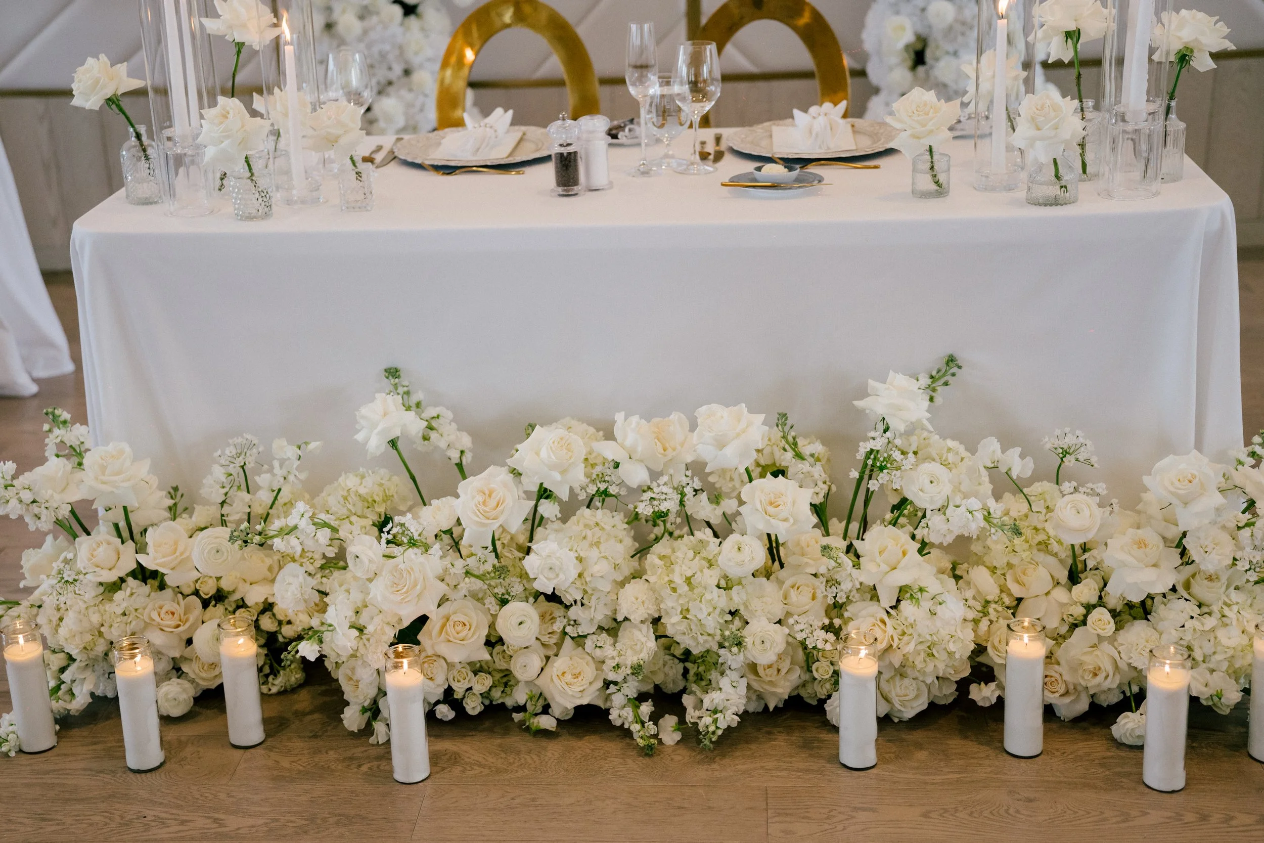 Wedding reception table decorated with white flowers, candles, and glassware.