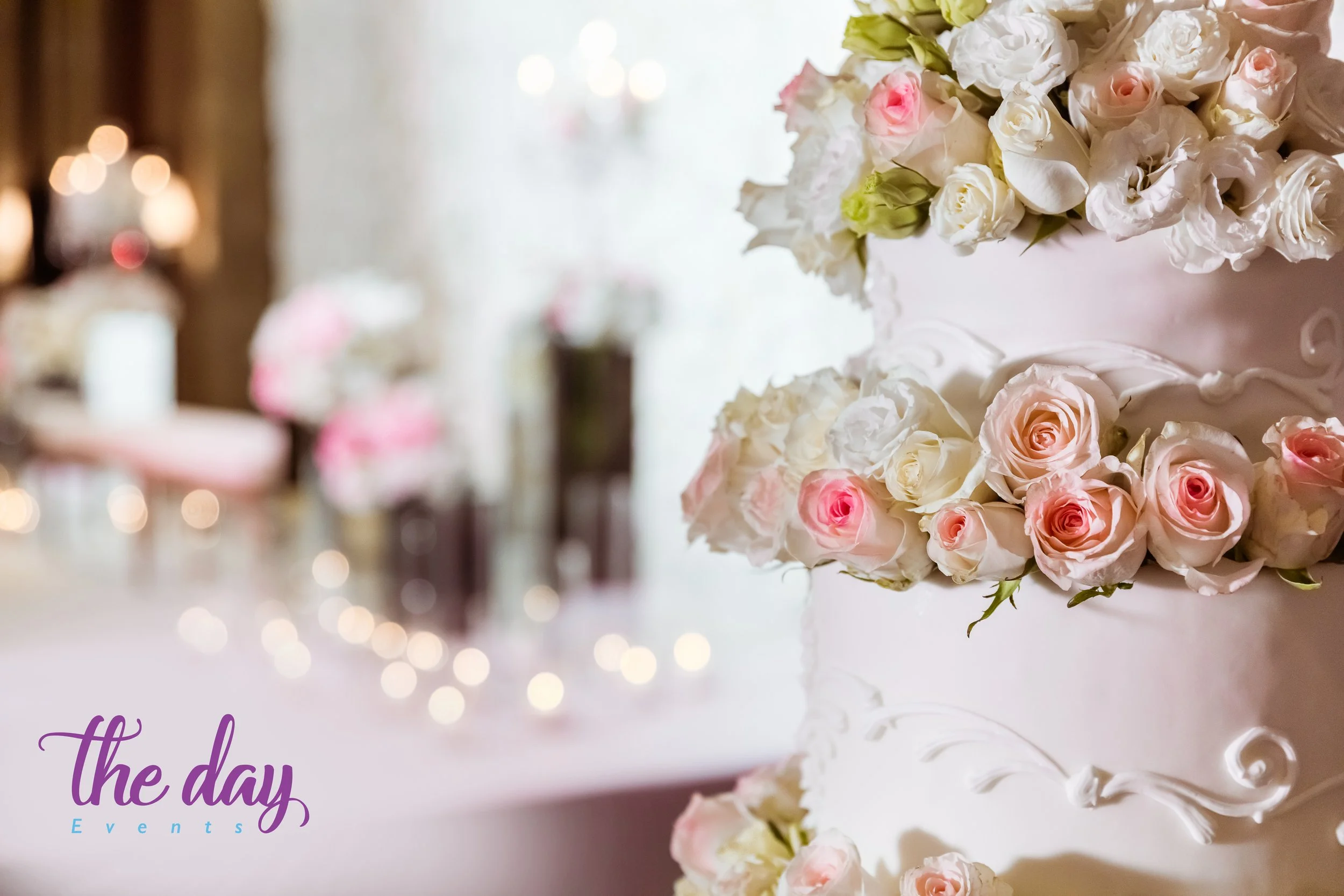 A multi-tiered wedding cake decorated with pink and white roses on a table at a celebration event.
